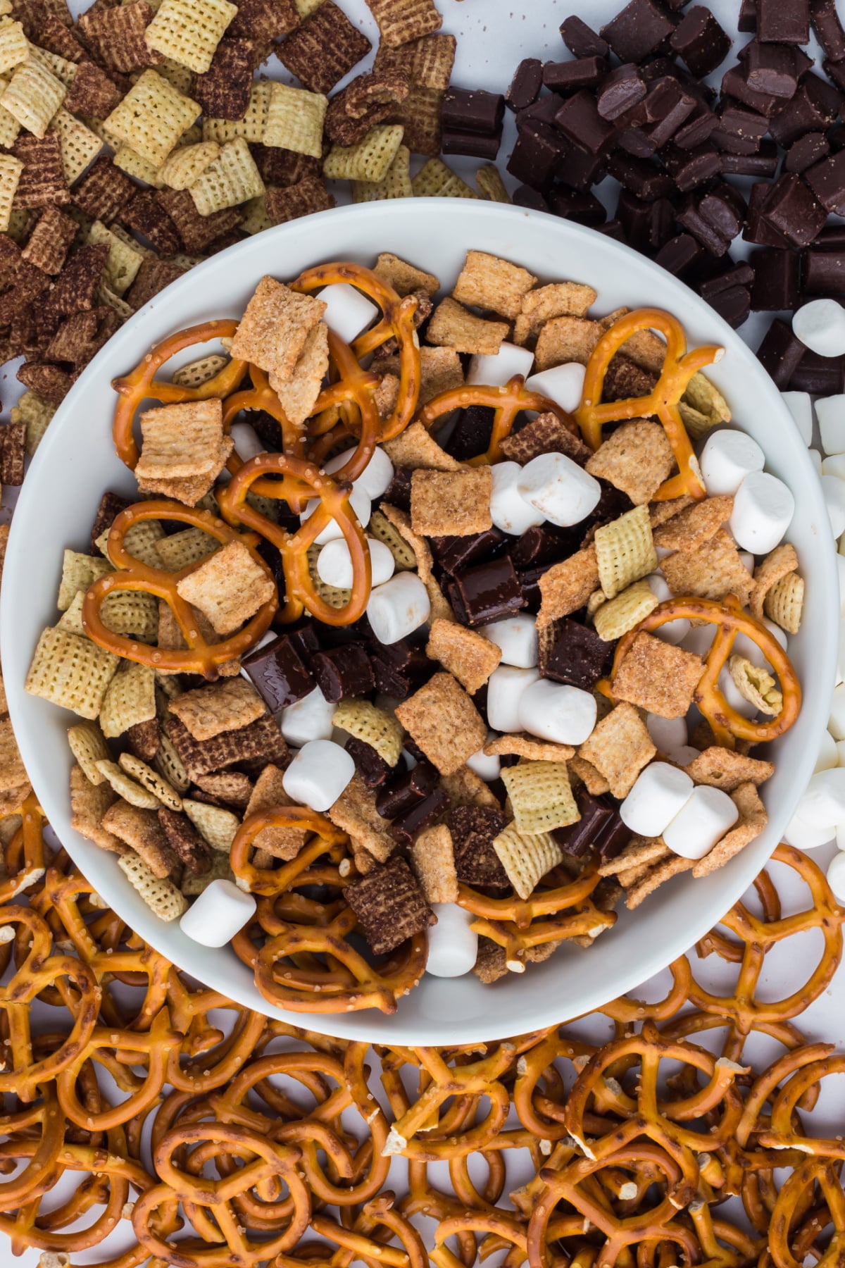 ingredients needed to make s'mores trail mix blended in a bowl surrounded by ingredients on a table