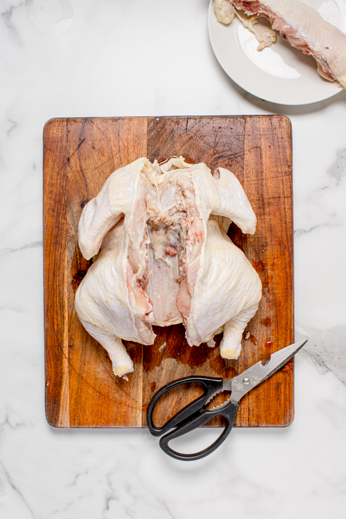 A whole chicken on a cutting board and the backbone taken out.