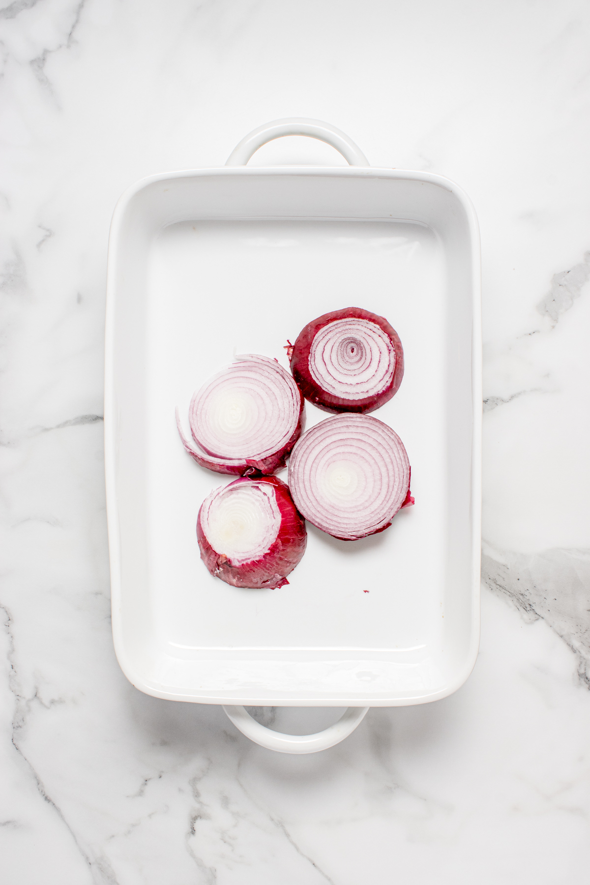 Onion slices on the bottom of a baking dish.