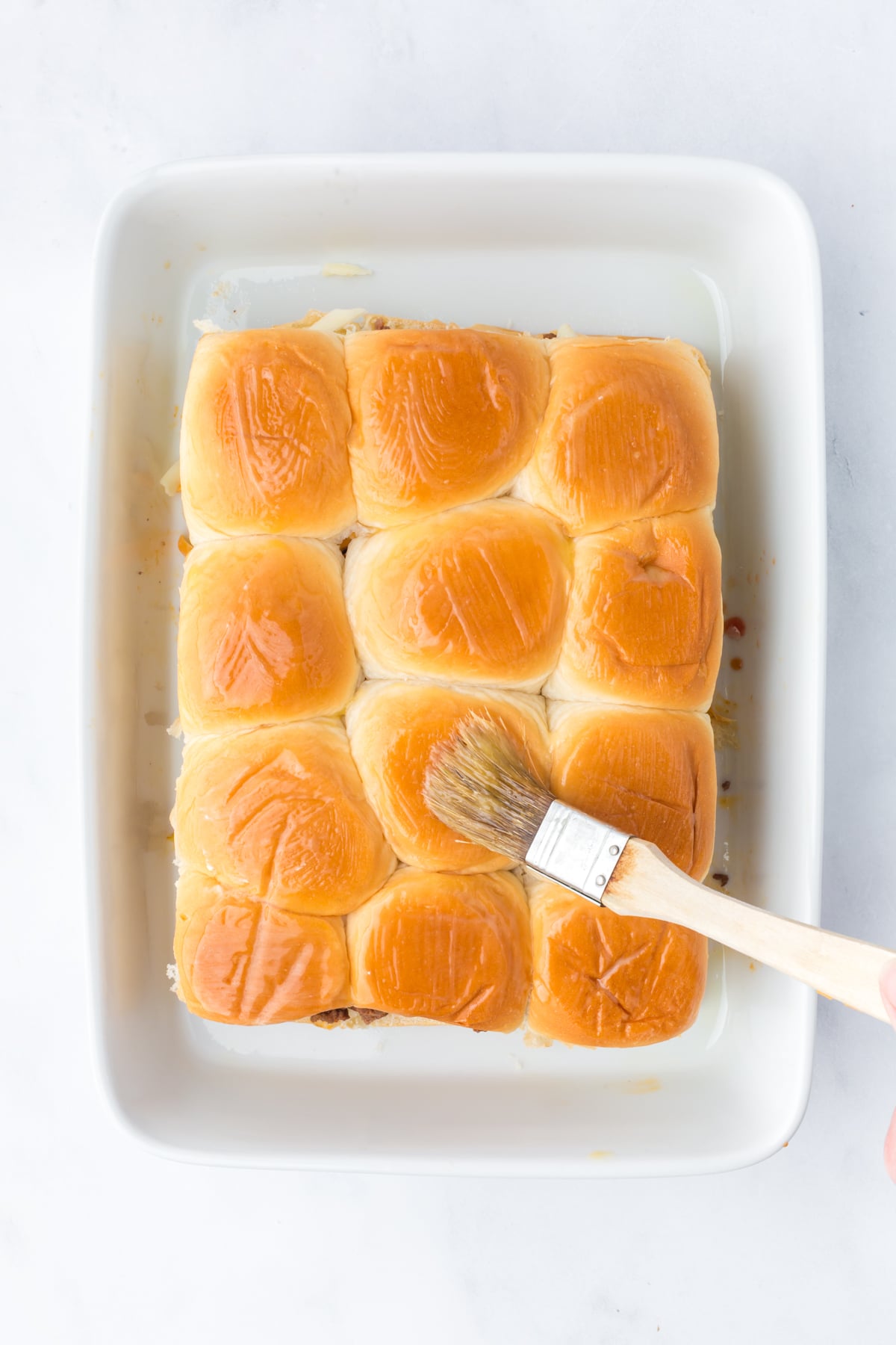 Melted butter and Worcestershire sauce being brushed over the bun tops.