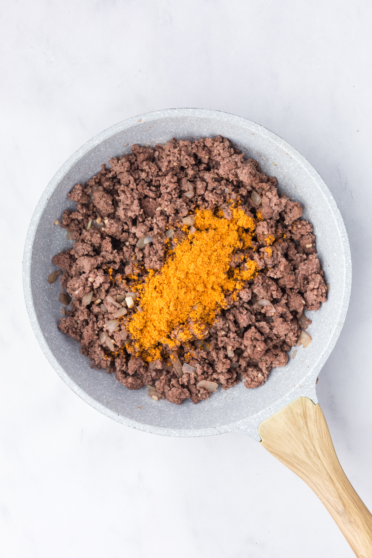 Cooked ground beef with taco seasoning on top in skillet.