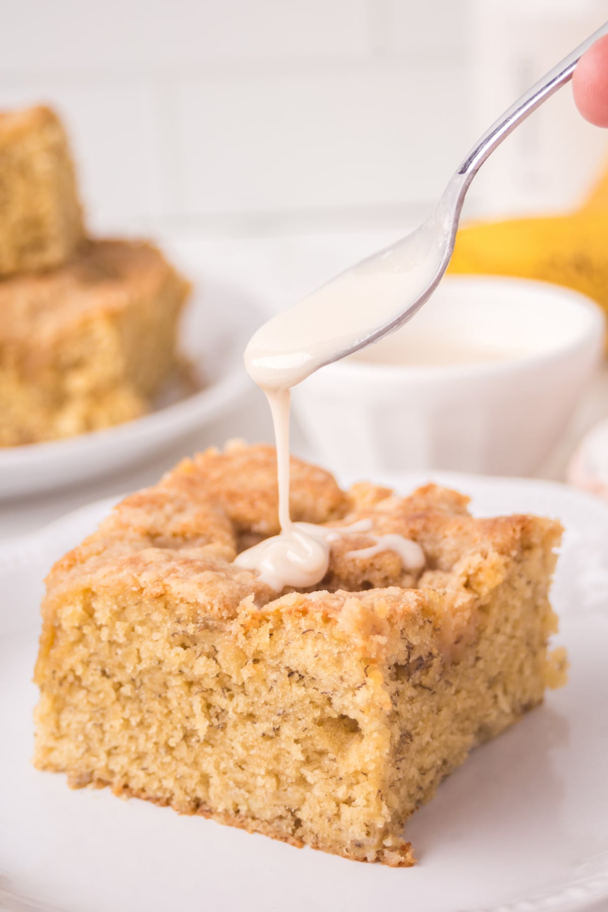 Spoonful of icing being drizzled on coffee cake slice on plate