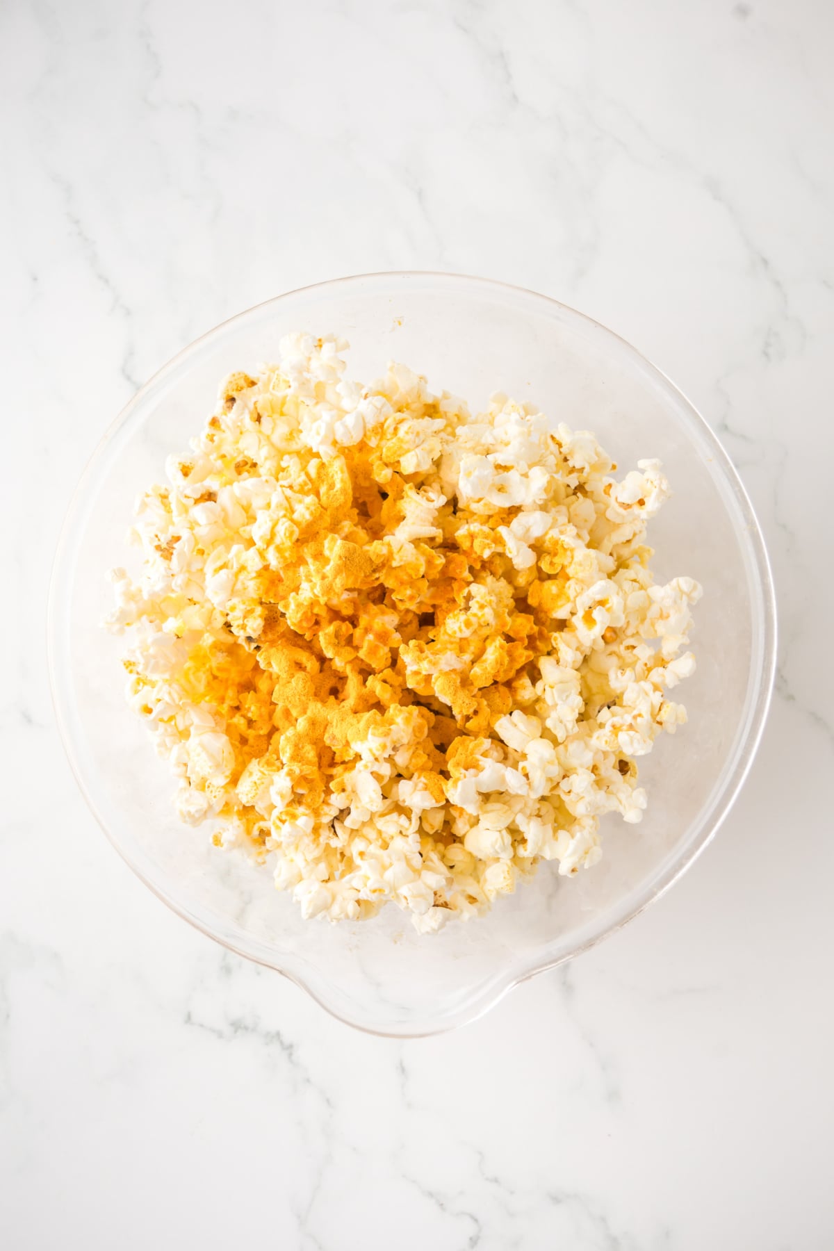 Popcorn in bowl with melted butter and cheese seasoning.