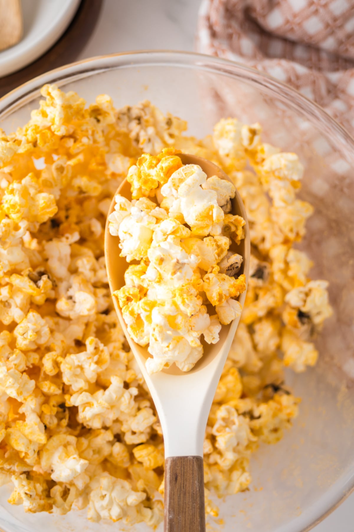 A wooden spoonful of popcorn held above a bowlful.