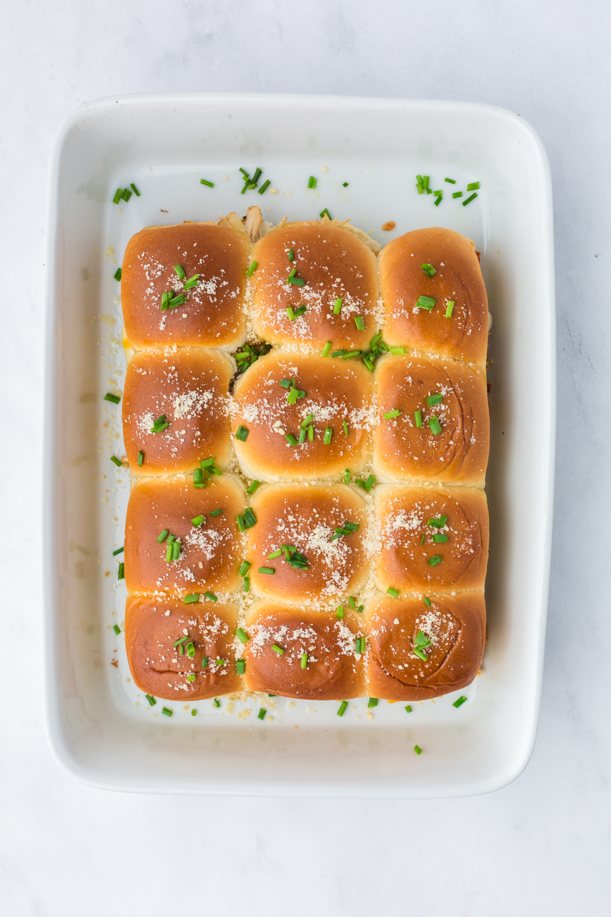 Parmesan cheese and chives are added to tops of baked sliders.