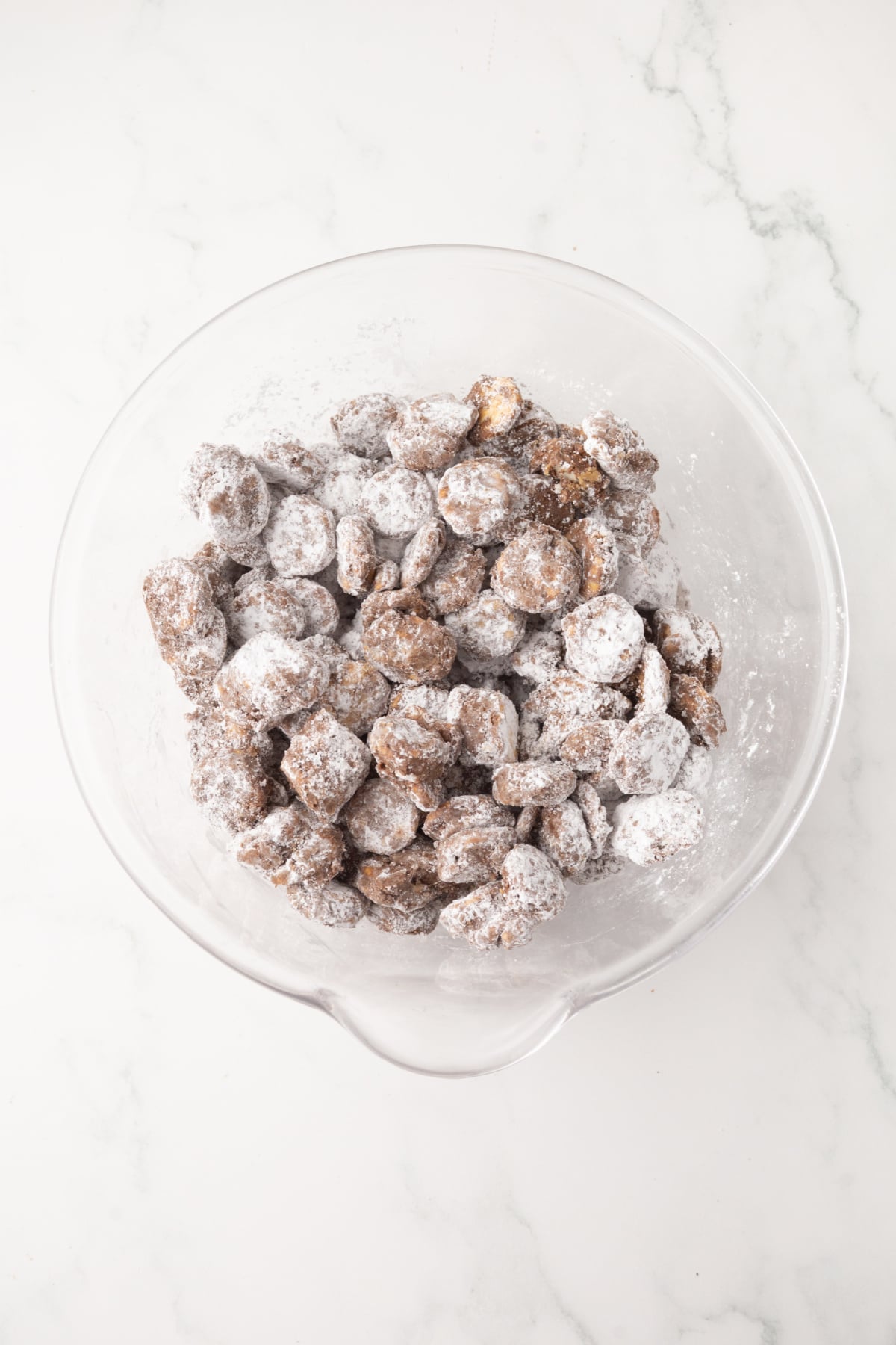 tossed muddy buddies fully coated in powdered sugar in bowl
