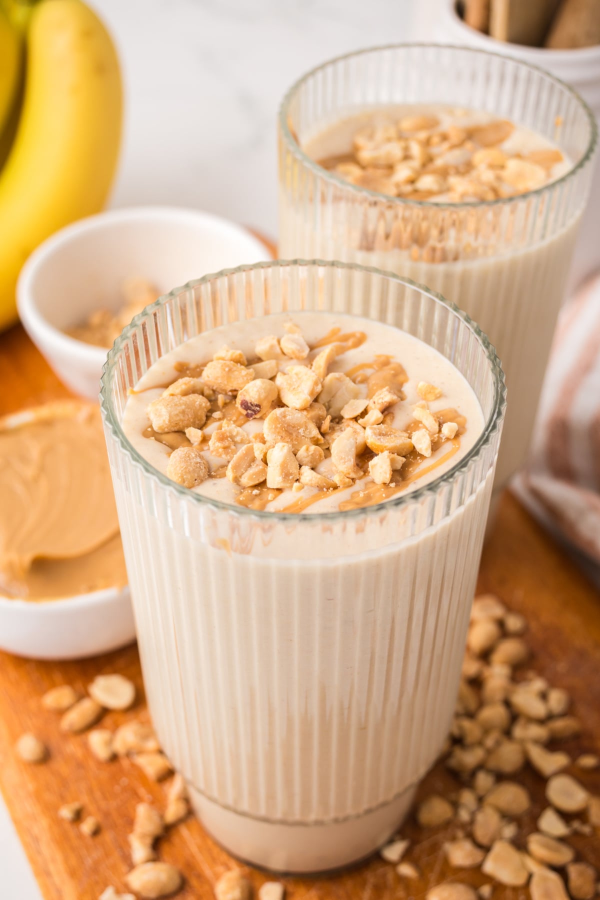 Two banana peanut butter smoothies in glass with chopped nuts on top on table
