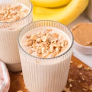 2 banana peanut butter smoothies in glass on table with bananas in background