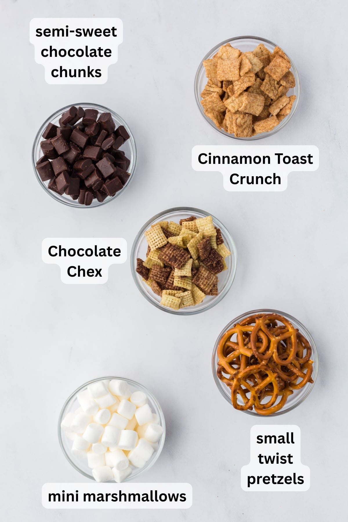 All the ingredients needed to make S'Mores Trail Mix in bowls on a table