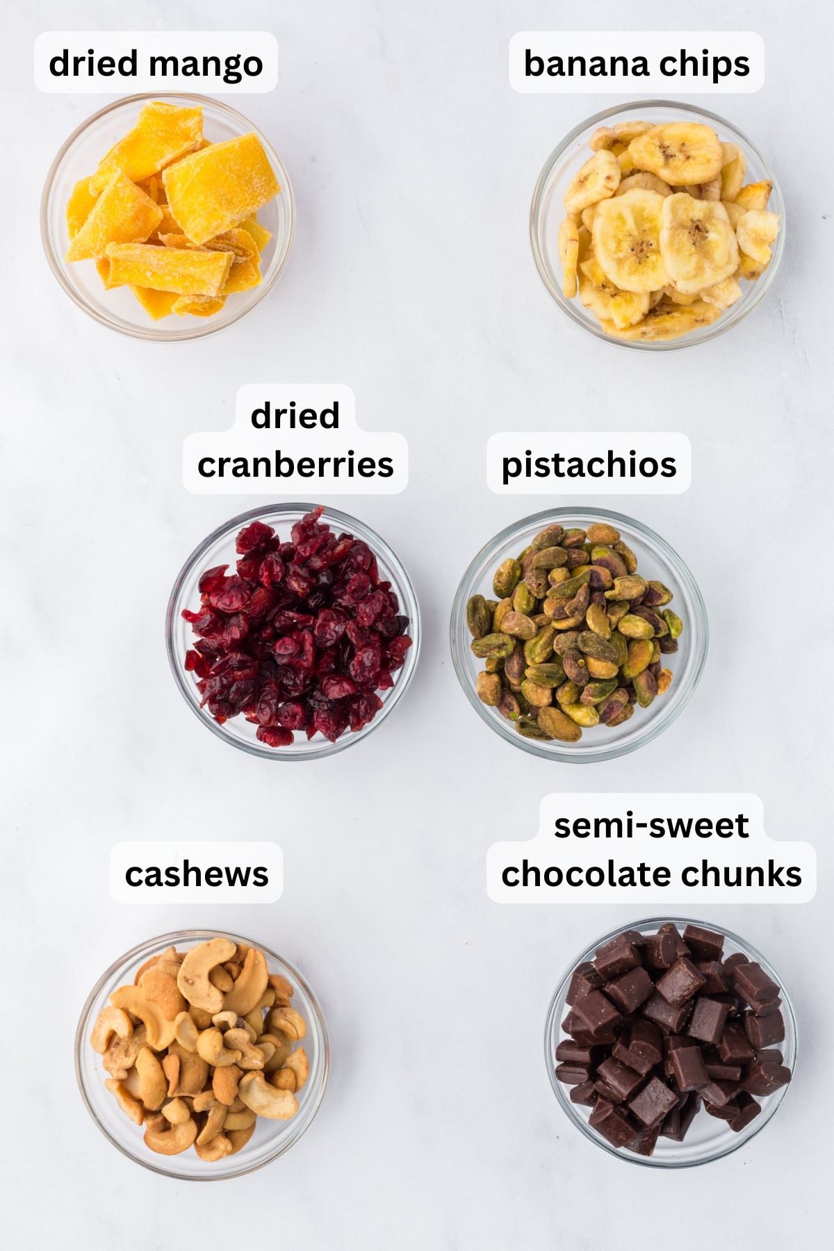 All the ingredients needed to make Tropical Trail Mix in bowls on a table