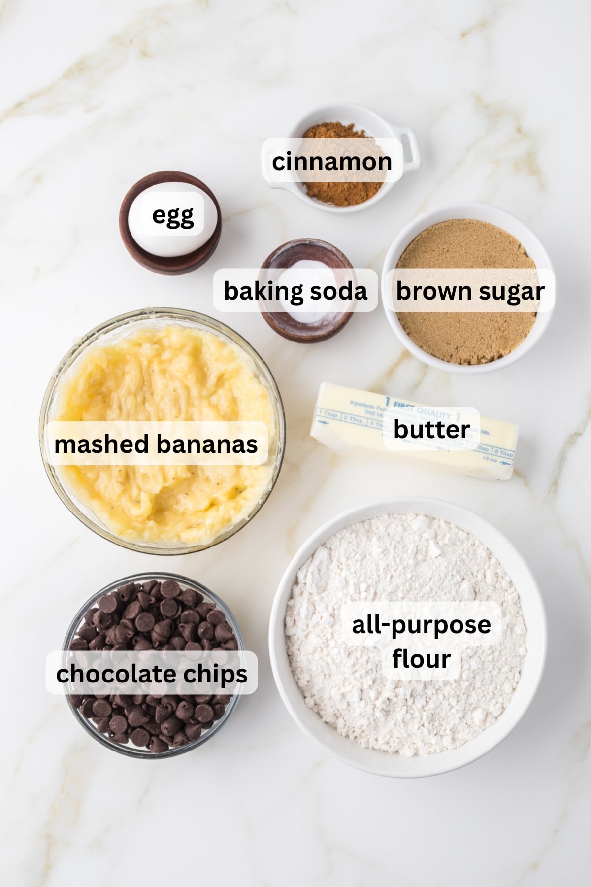 All of the ingredients for banana bread cake including ripe bananas flour butter sugar and chocolate chips in bowls on table
