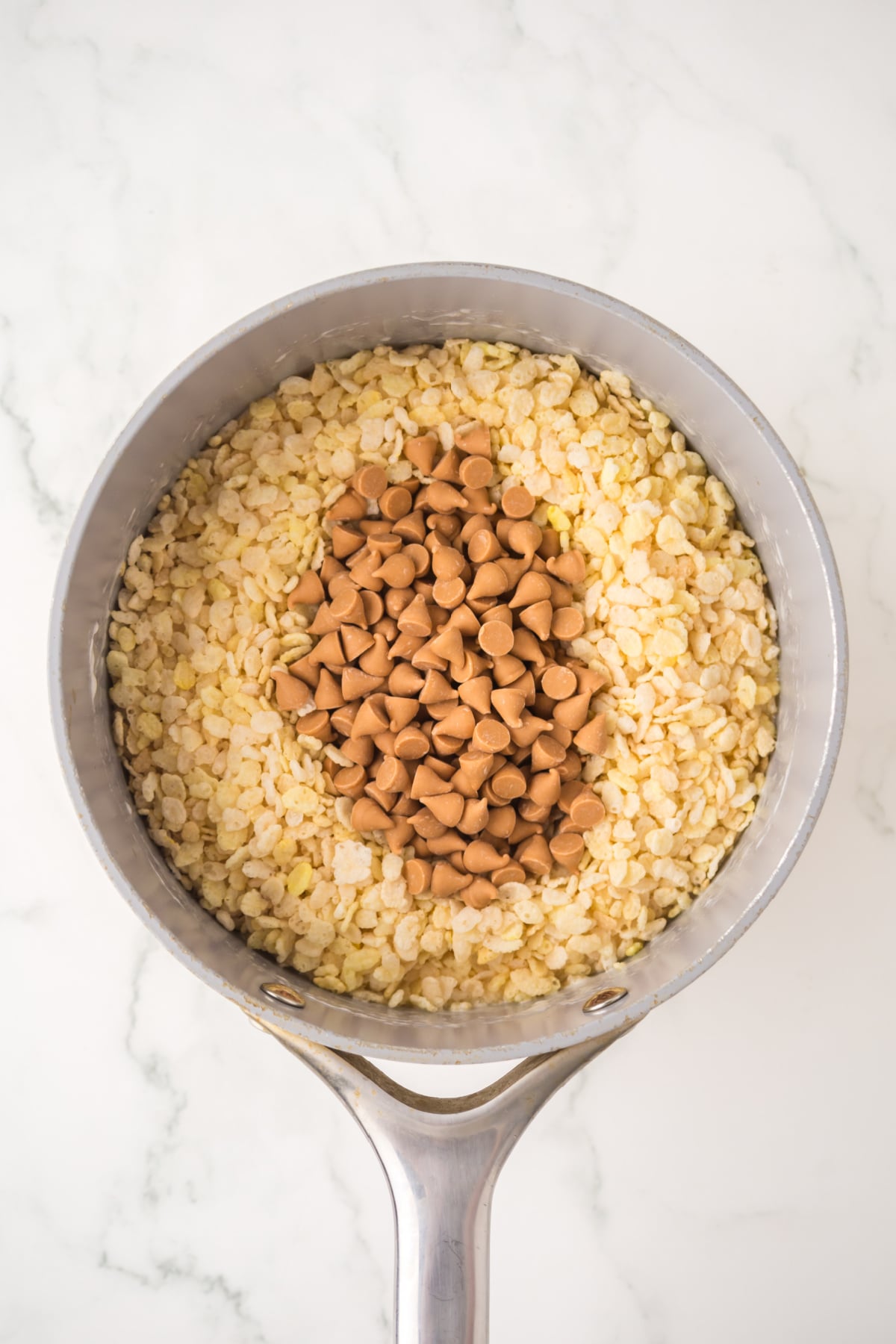 A saucepan full of melted butter and marshmallows with cereal and butterscotch chips added off heat