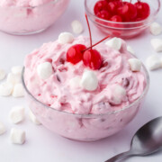 A bowl of cherry fluff salad topped with 2 cherries on a table.