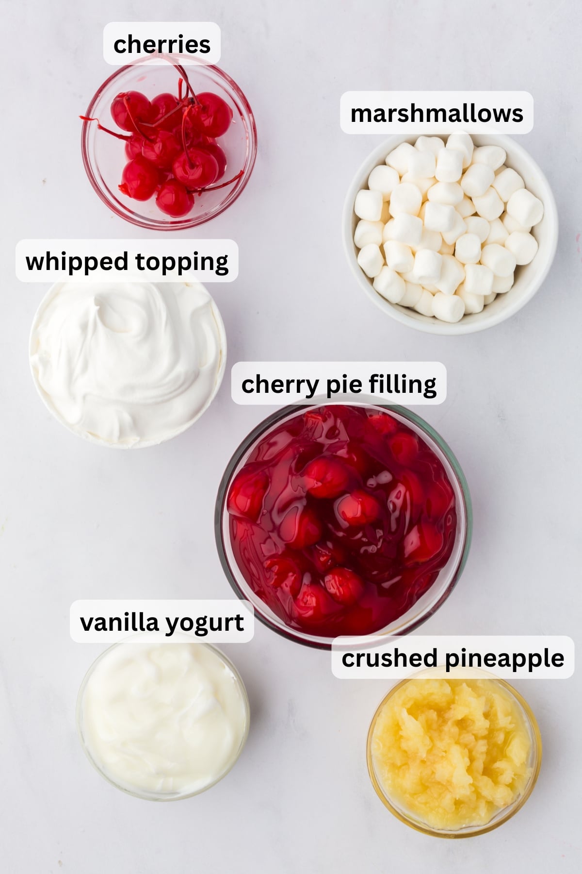Ingredients to make this fluff salad with cherries in bowls on a table.