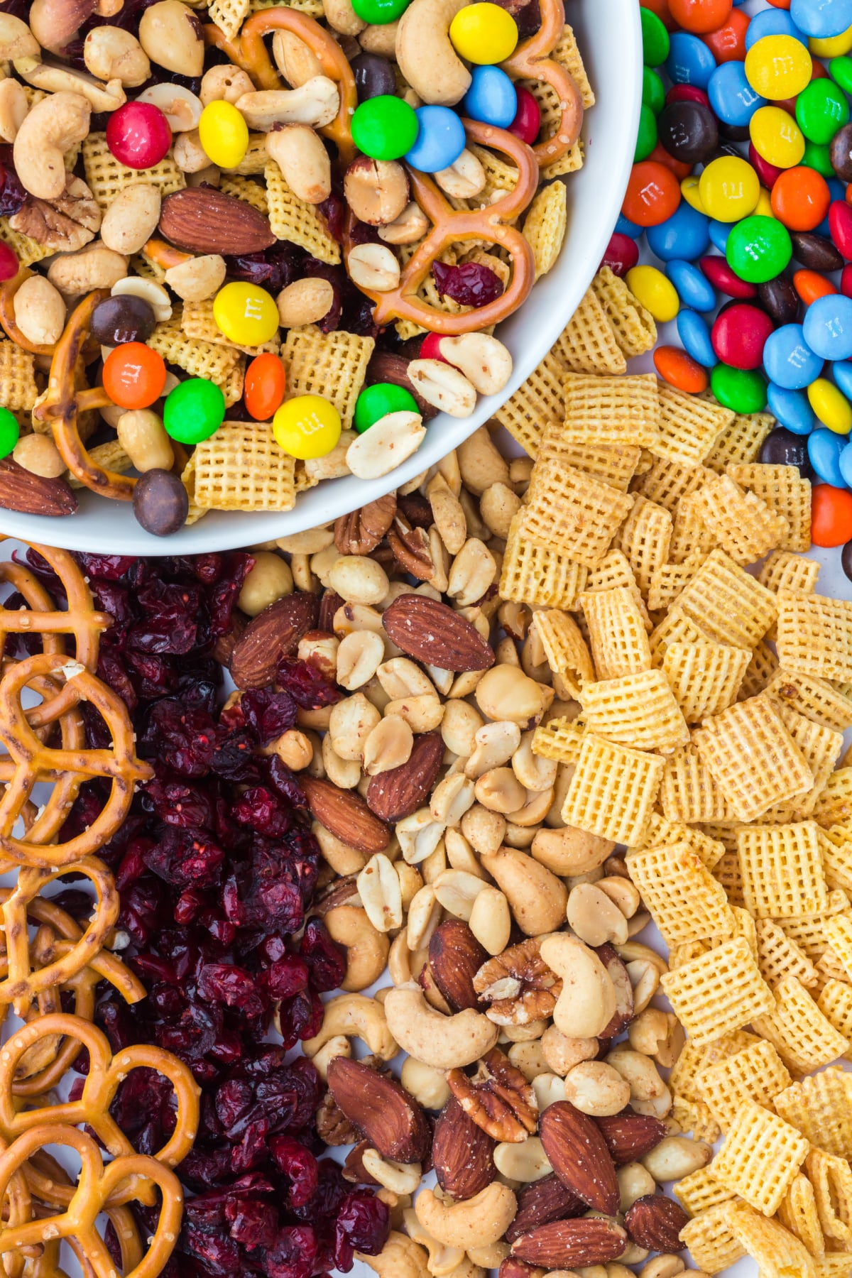 A bowl of trail mix surrounded by cereal on table