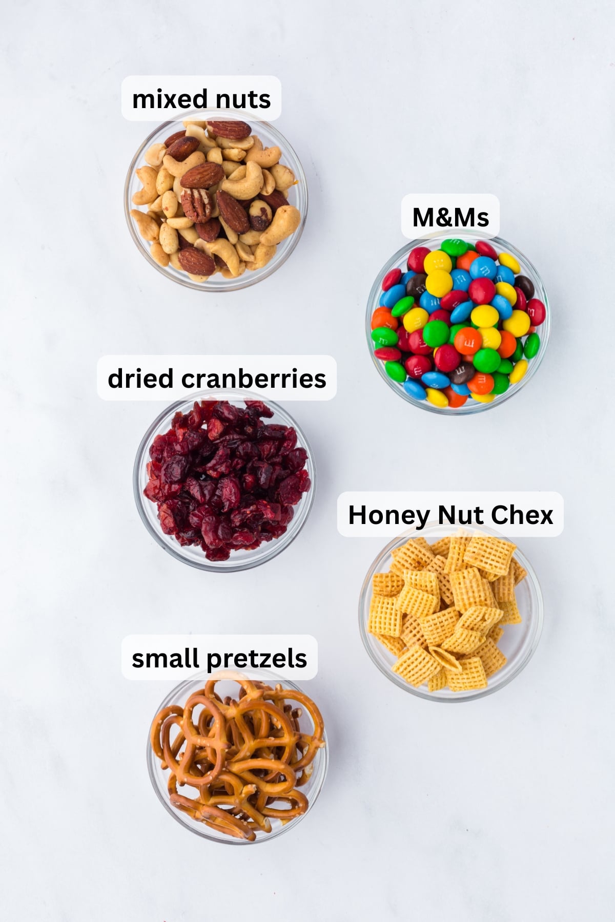 ingredients for classic trail mix including cereal pretzels nuts cranberries and chocolate candies in bowls on table