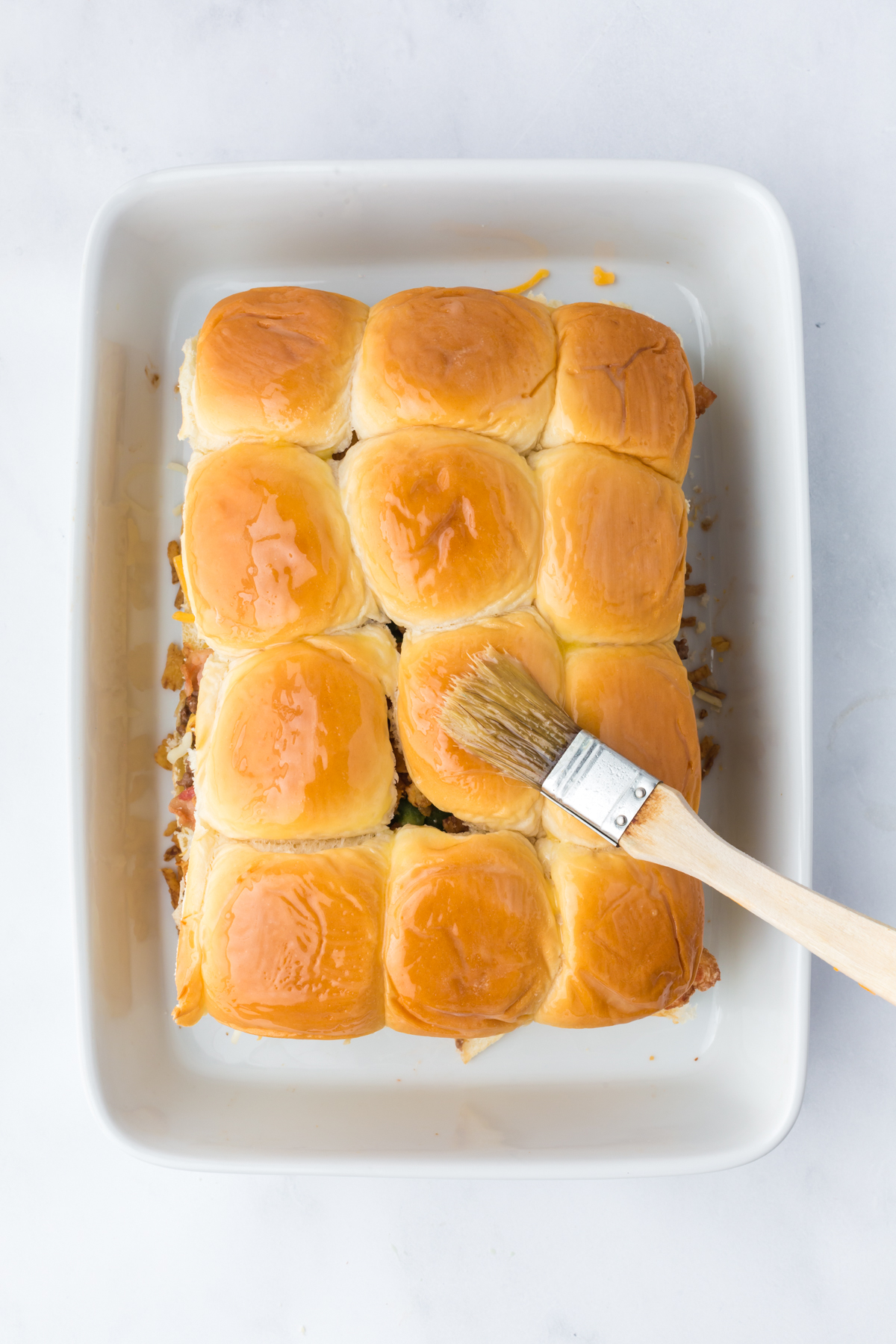 melted butter with Dijon mustard and Worcestershire sauce being brushed on top of sliders before baking.