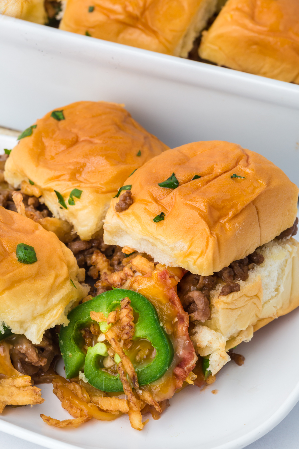 Sliders inside baking dish with melted cheese pulled out and a jalapeno on top.