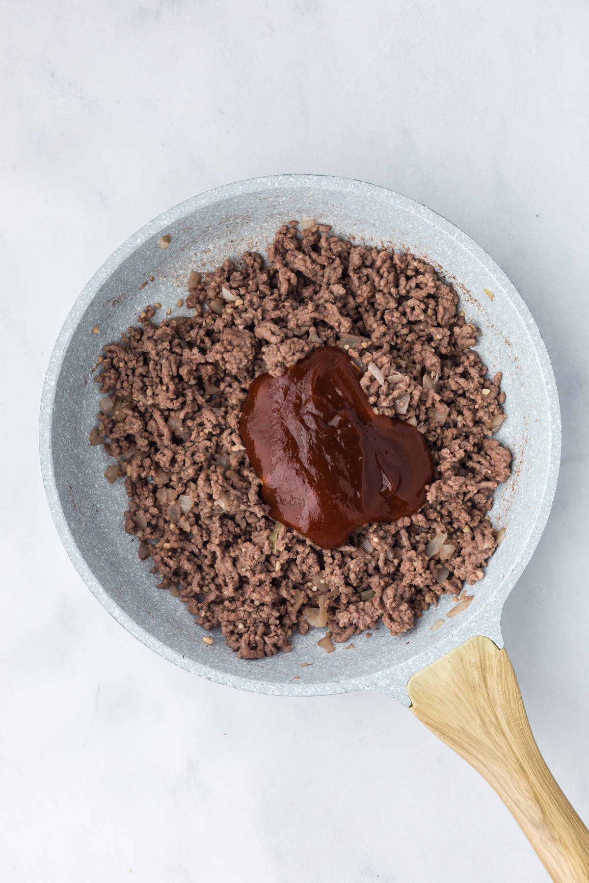 Cooked ground beef in skillet with BBQ sauce added.