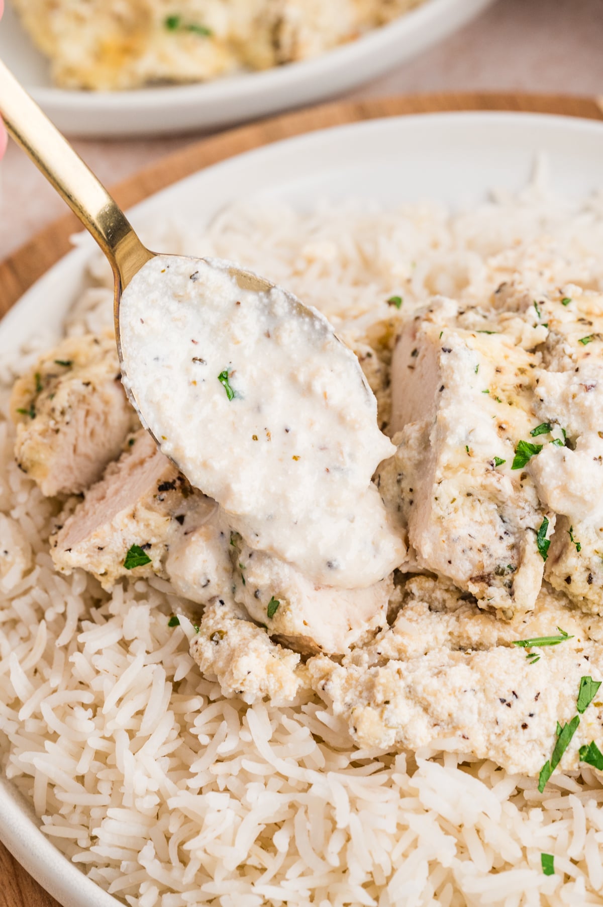 A spoonful of sauce being drizzled on top of a sliced chicken breast on top of rice