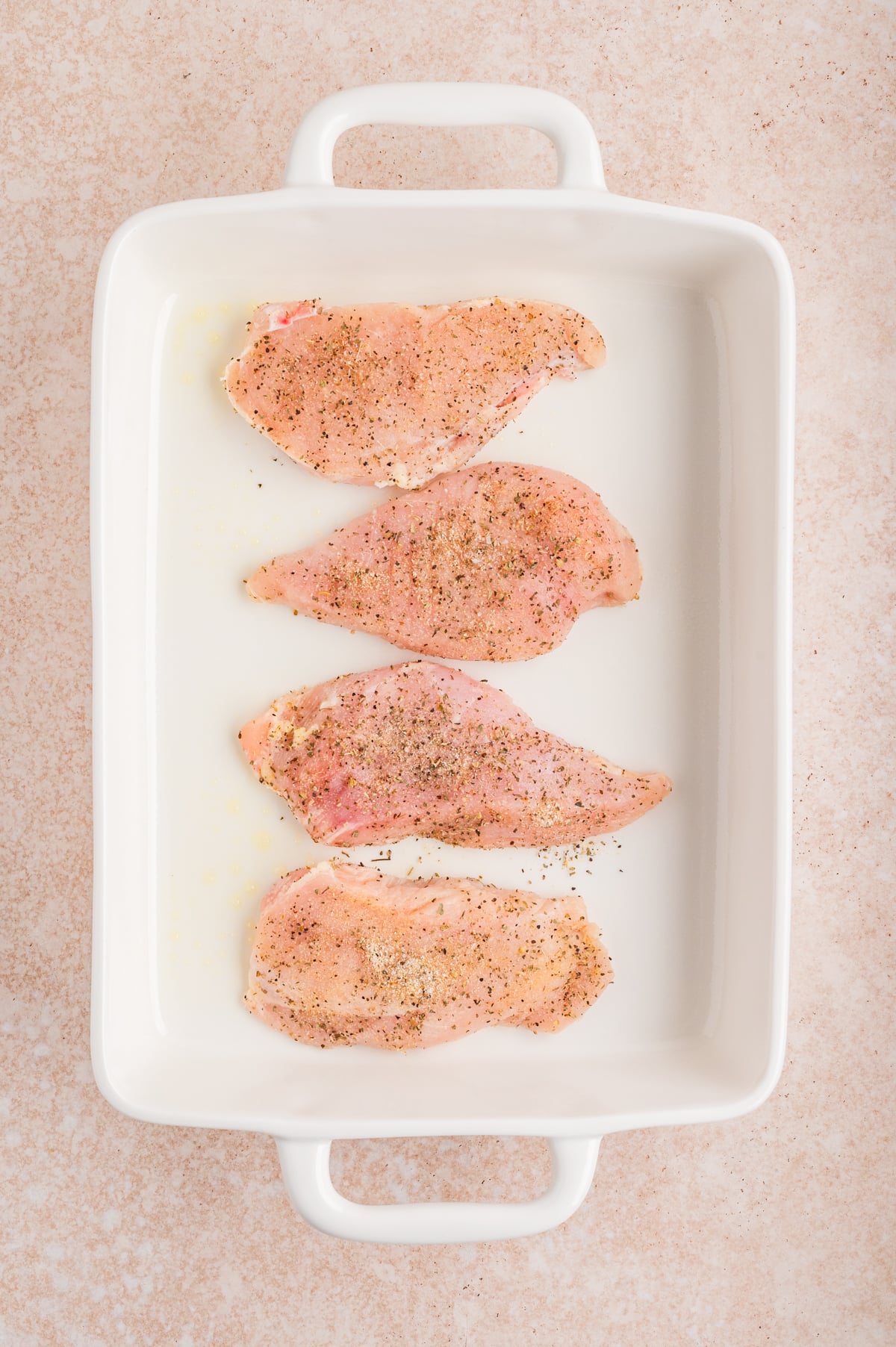 chicken breasts in baking dish covered in half of seasoning mixture.