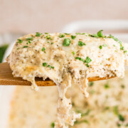 A piece of sour cream chicken lifted out of the baking dish on a spatula.