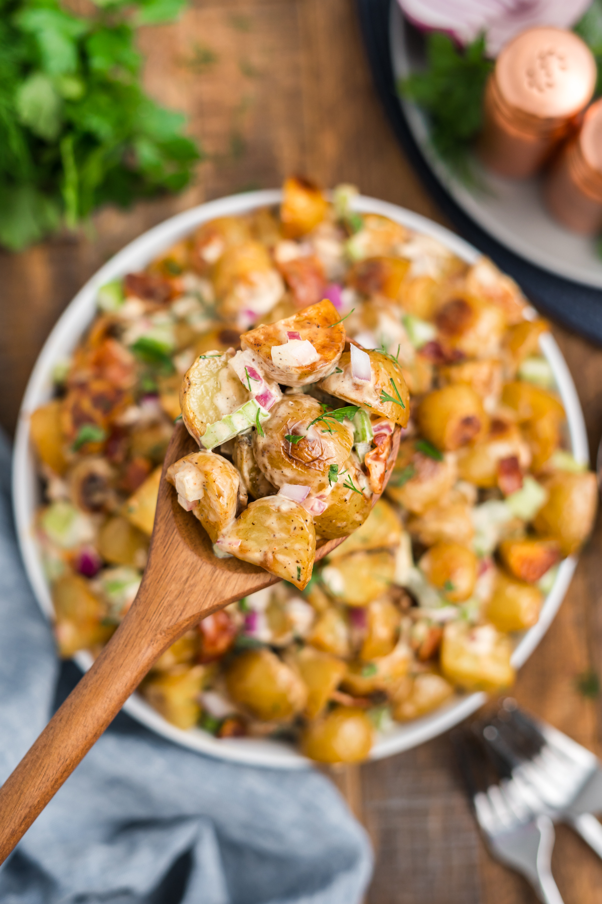 Wooden spoon lifting crispy potato salad recipe from a serving bowl