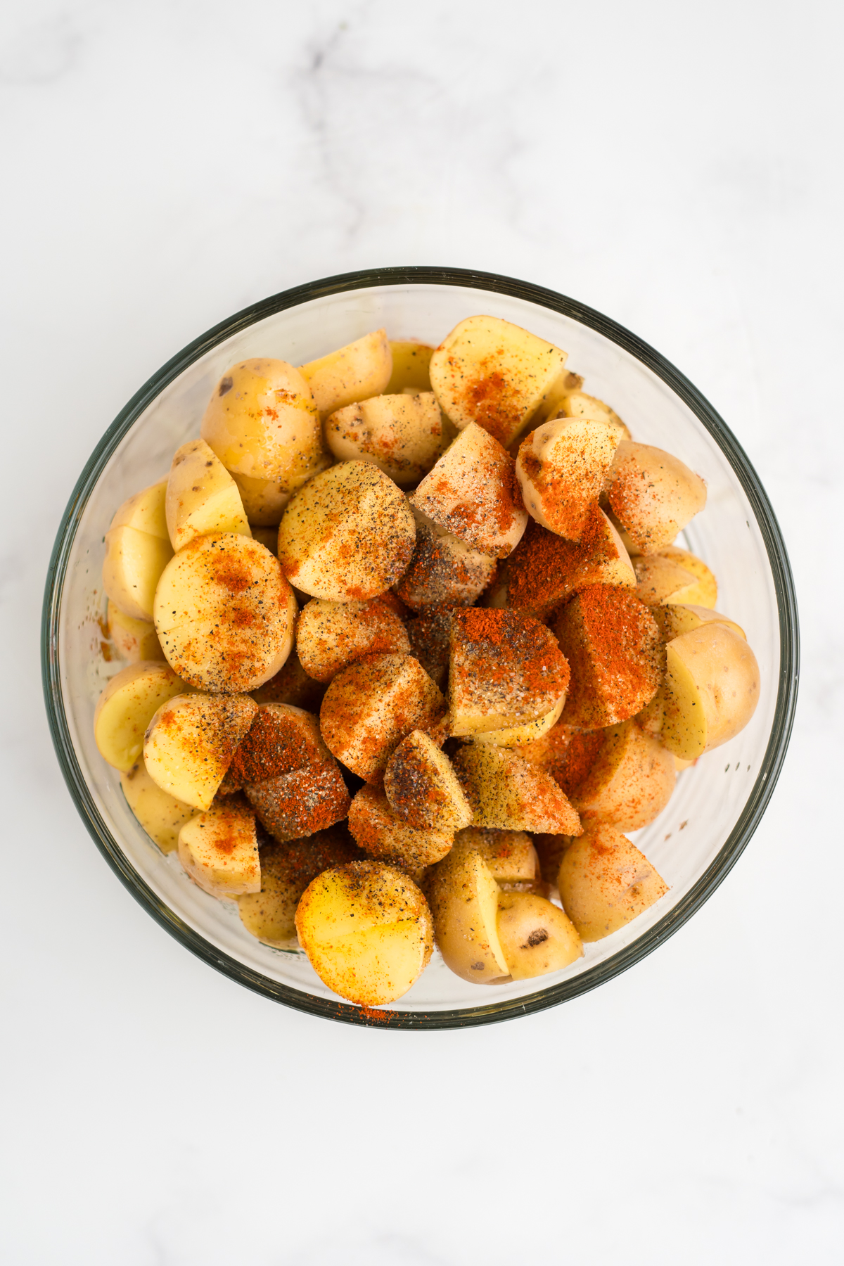 washed potatoes in a bowl with olive oil, salt, pepper, garlic powder, and paprika.