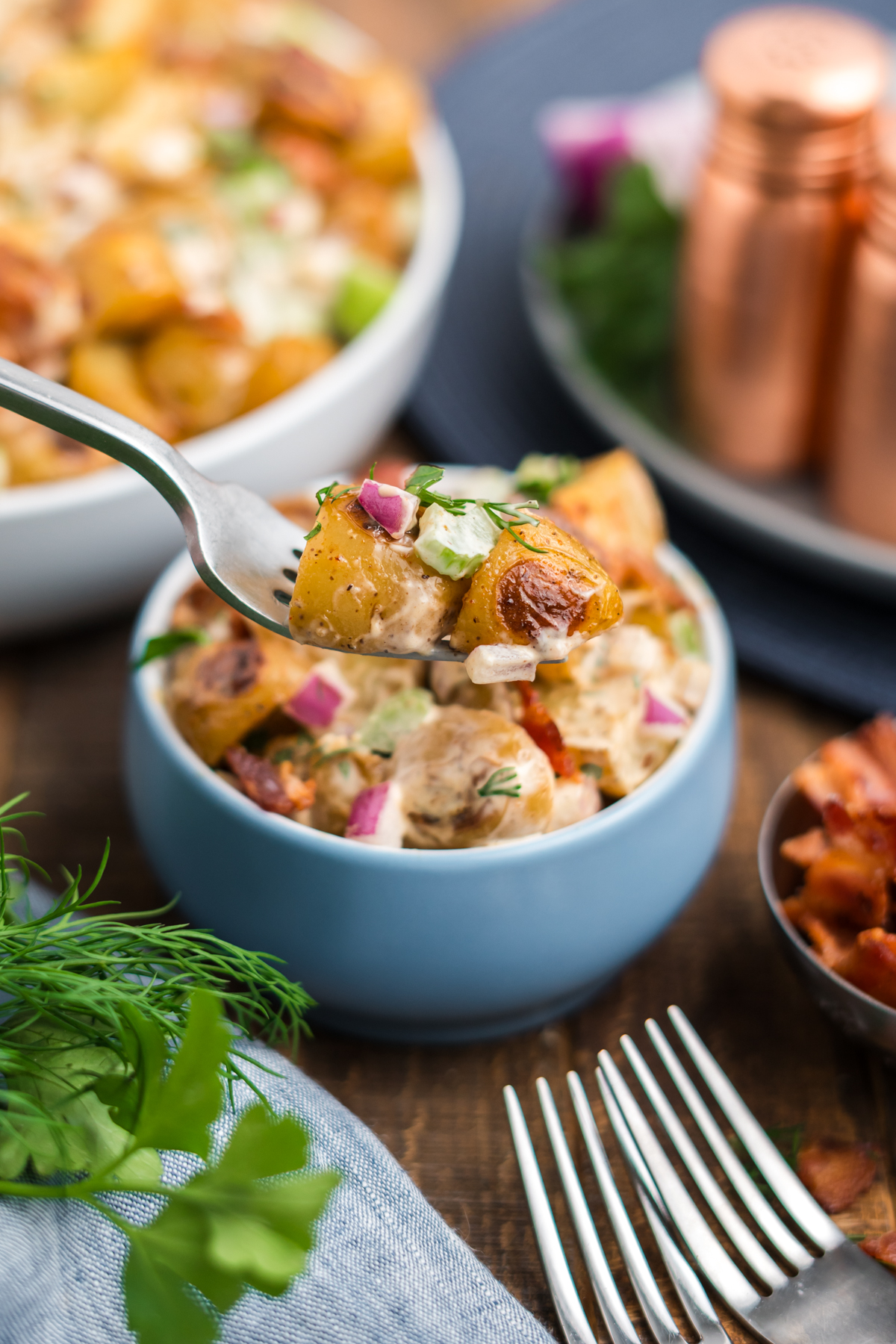Fork holding a bite of roast potato salad above serving bowl
