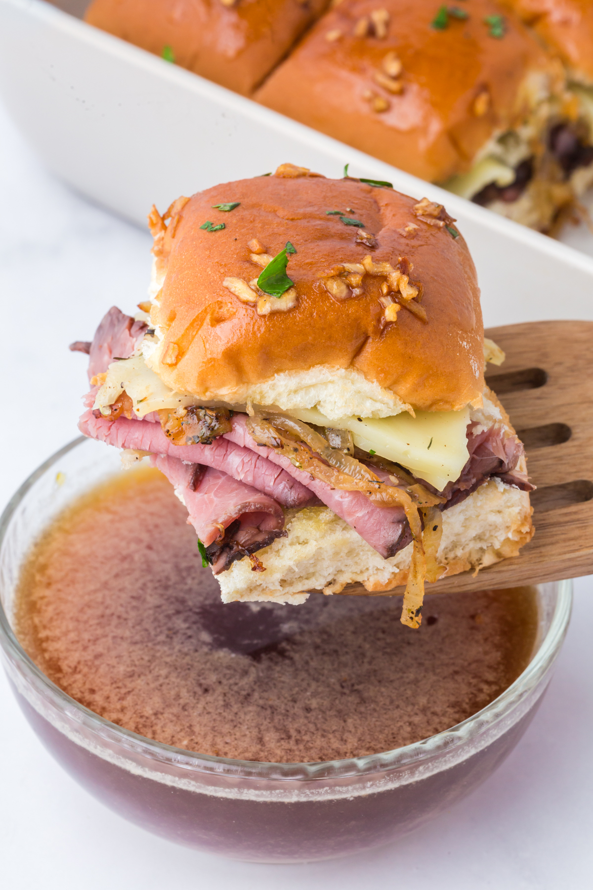 A slider being served on a spatula above some au jus in a small bowl.