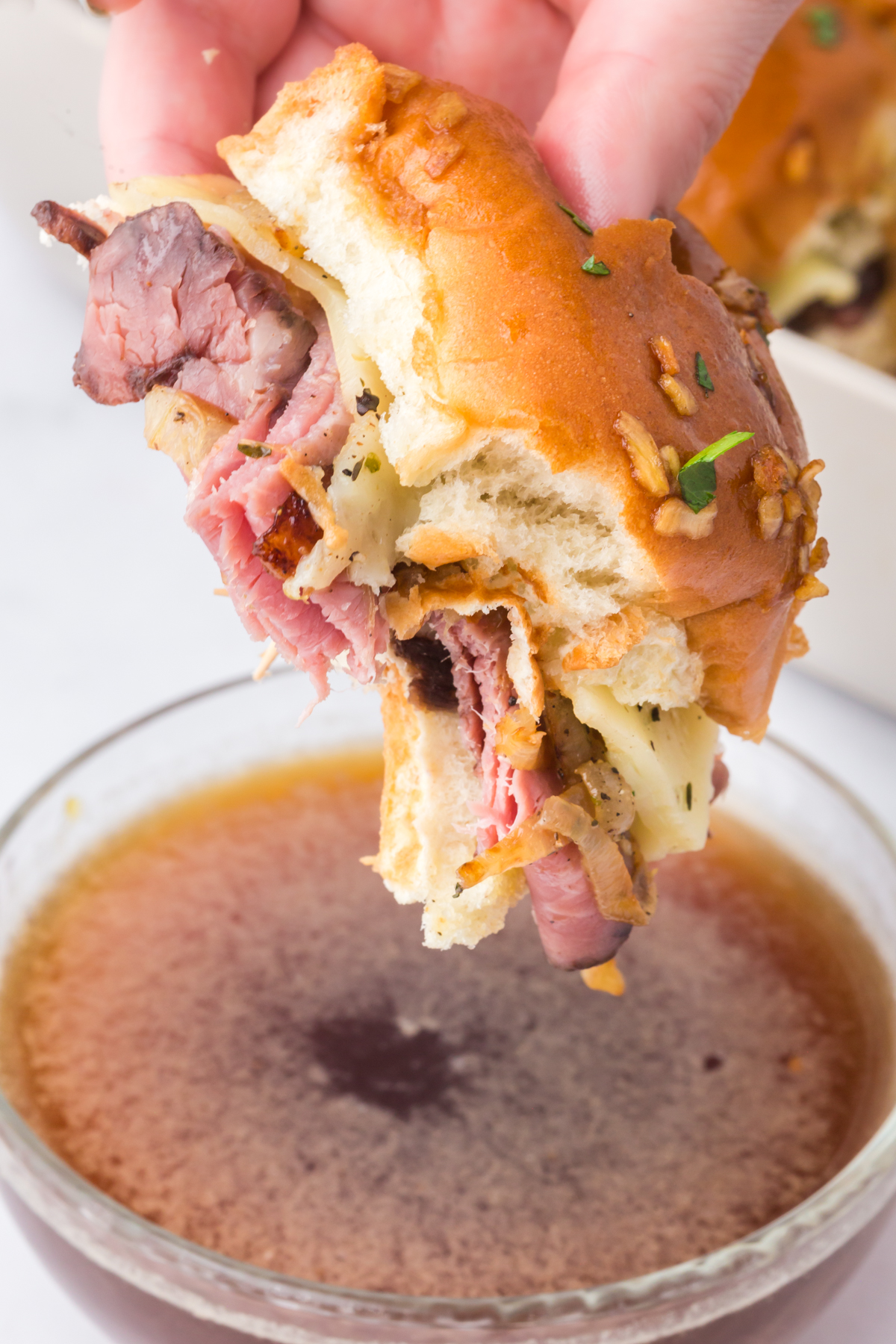 A slider missing a bite being dipped into the au jus.