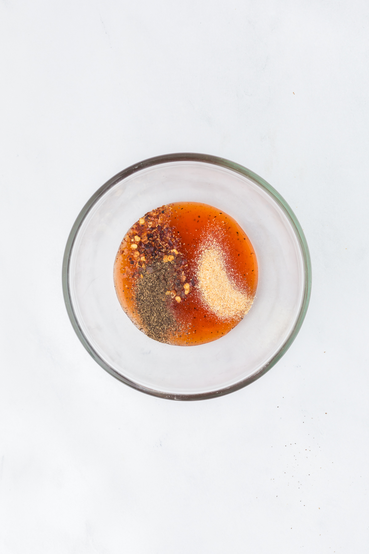 A bowl with hot honey, red pepper flakes, salt, black pepper, and garlic powder. 