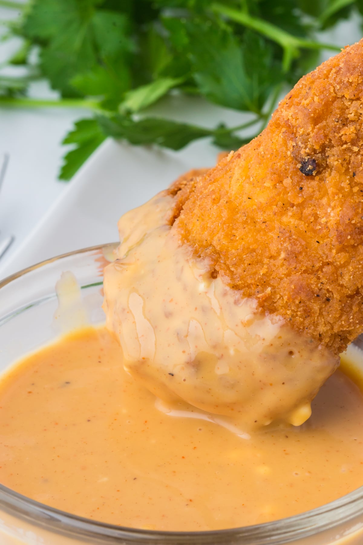 A chicken tender dipped in a bowl of hot honey mustard sauce on a table