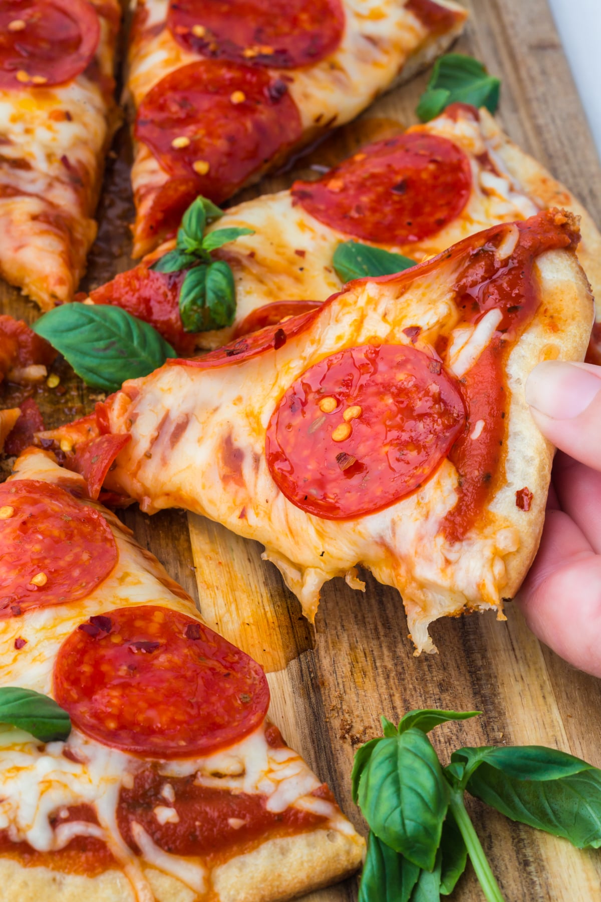 Pepperoni Pizza drizzled with hot honey on cutting board with a slice being removed.