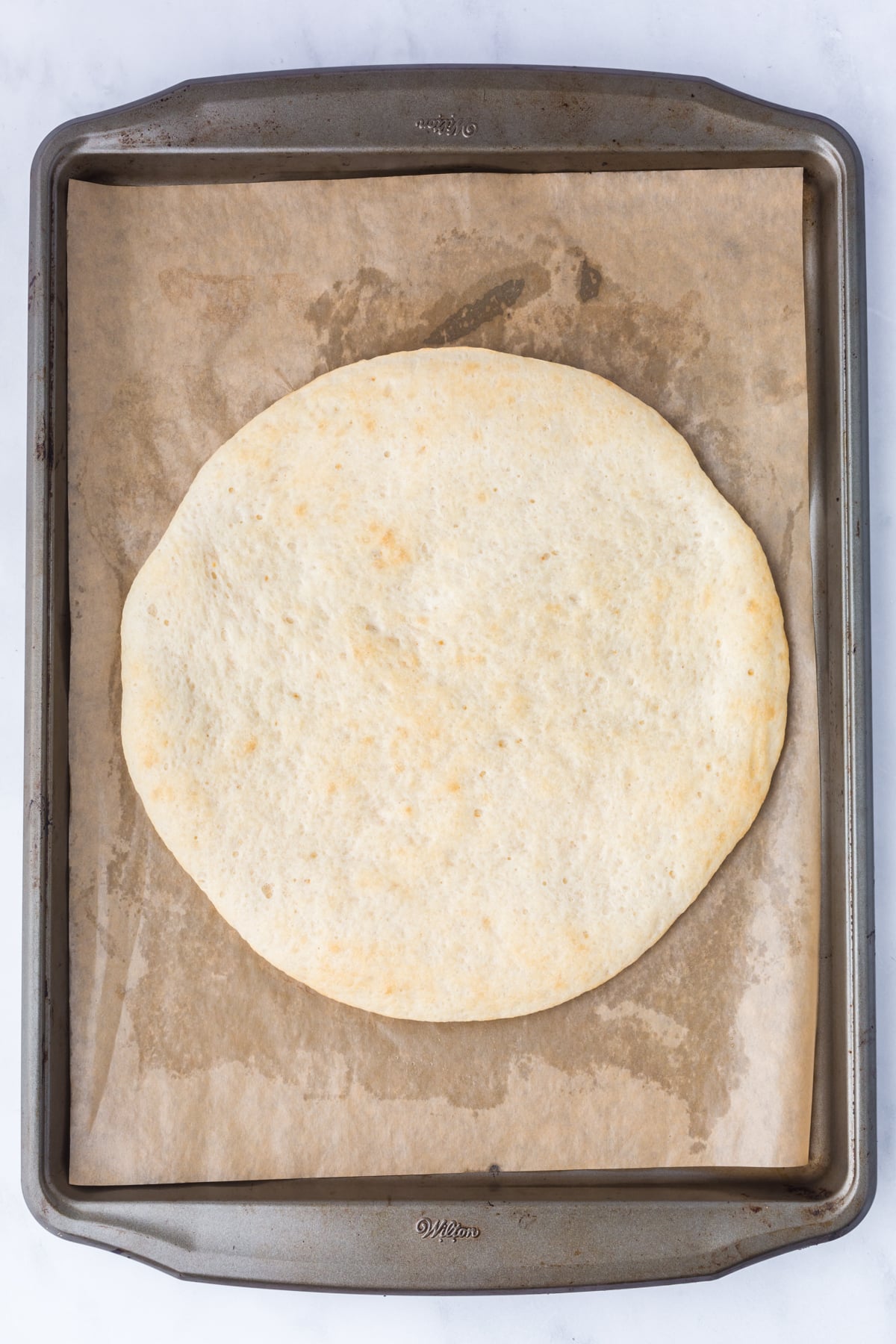 Pre-baked dough on a parchment covered baking sheet.