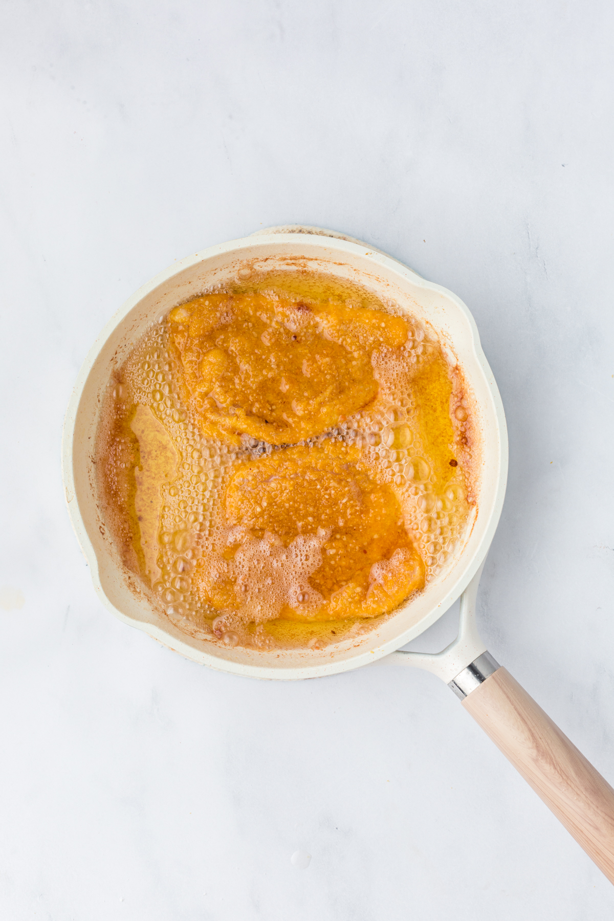 Two breaded chicken breasts being fried in oil in a saucepan.