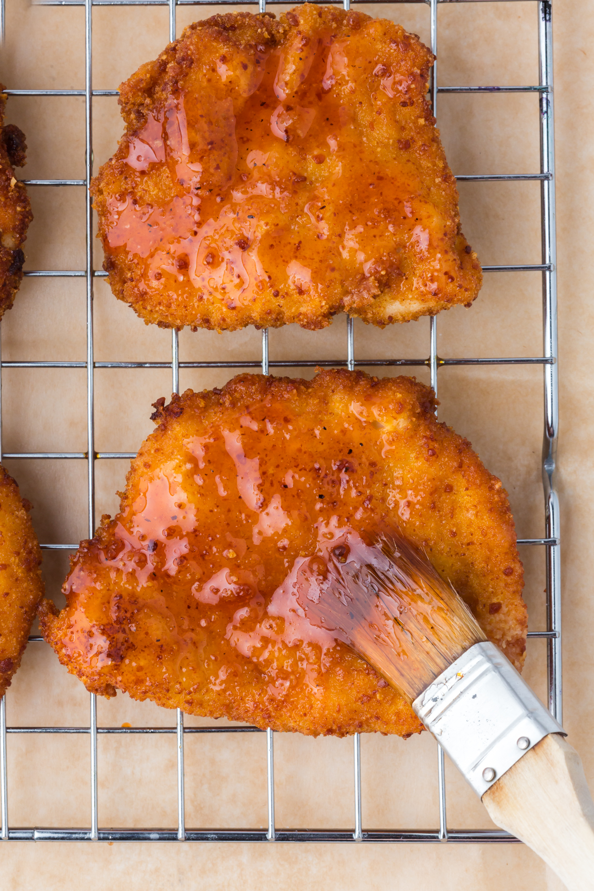 Freshly fried chicken on a rack being brushed with hot honey sauce.