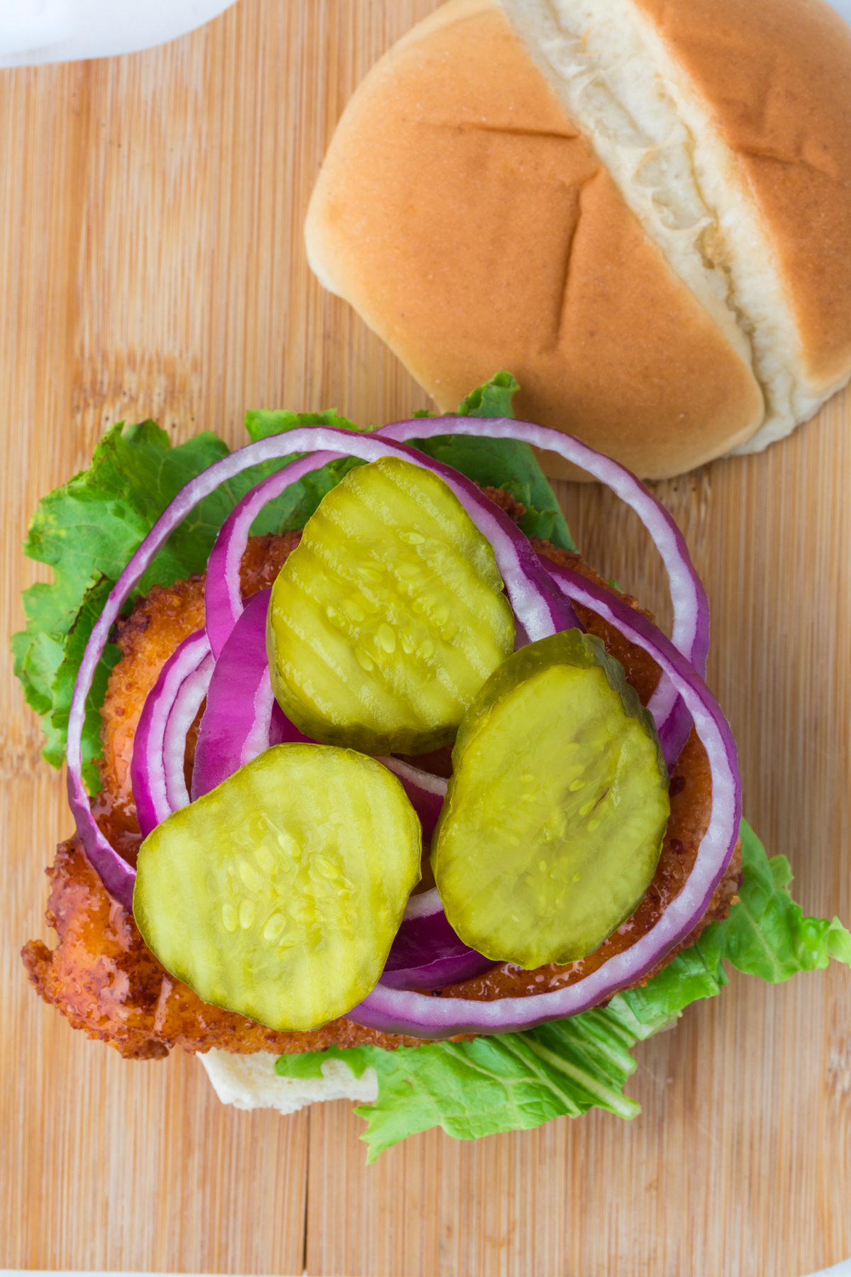 A lettuce, chicken, onion and pickle covered bun on a cutting board