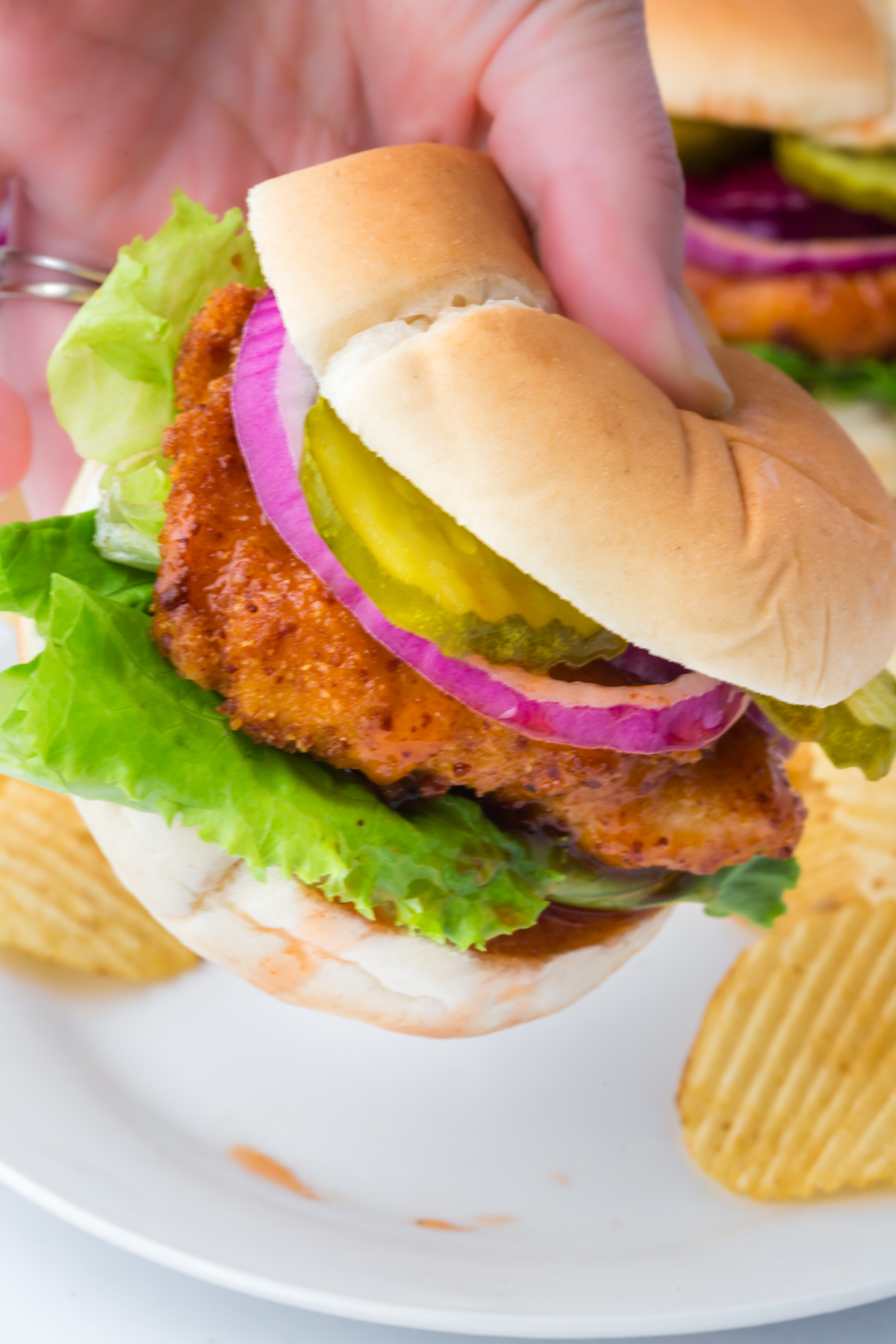 A chicken sandwich being lifted off a plate.