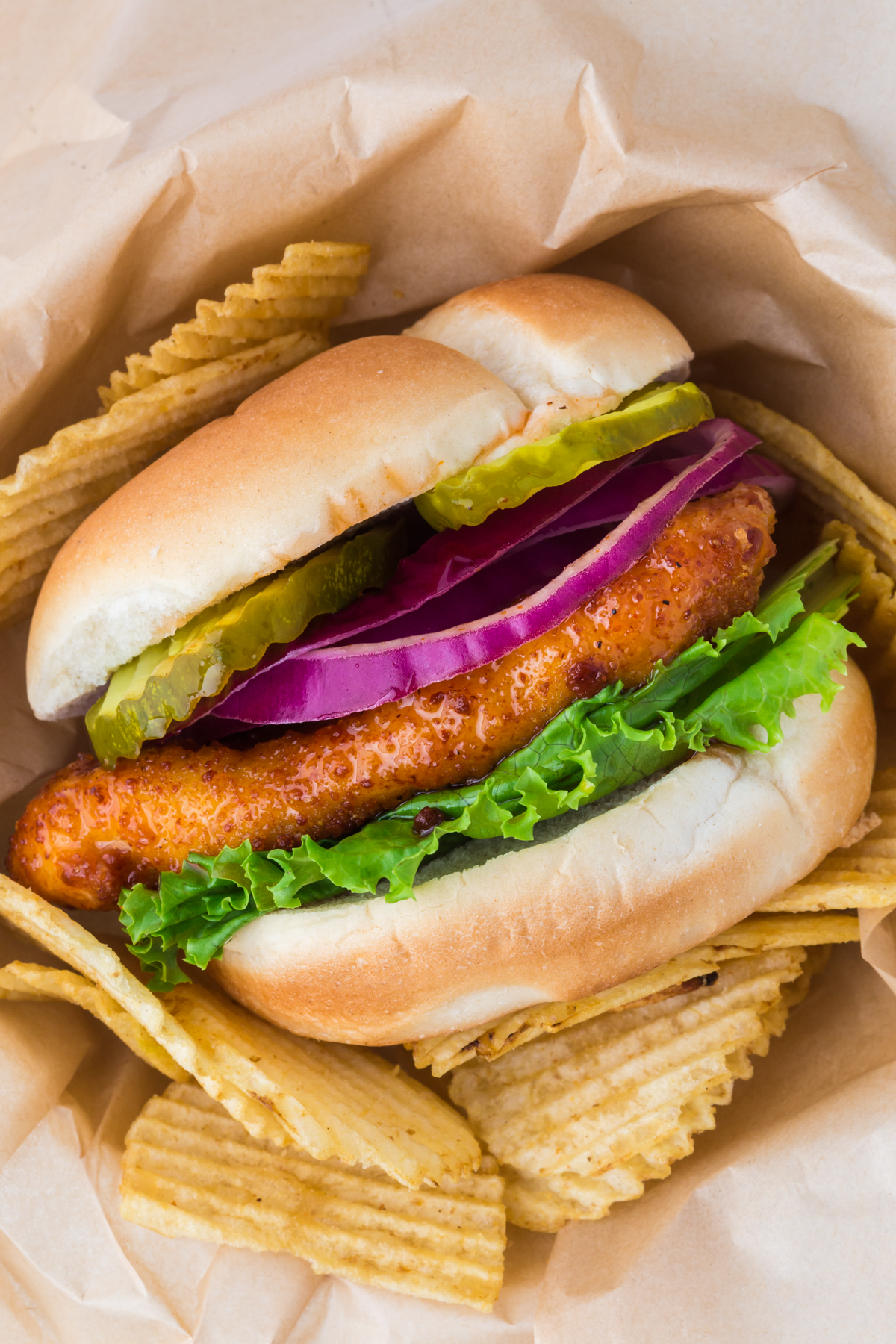 A chicken sandwich surrounded by some potato chips and parchment.