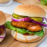 A Hot honey Chicken Sandwich with lettuce, pickles and onion on a cutting board.