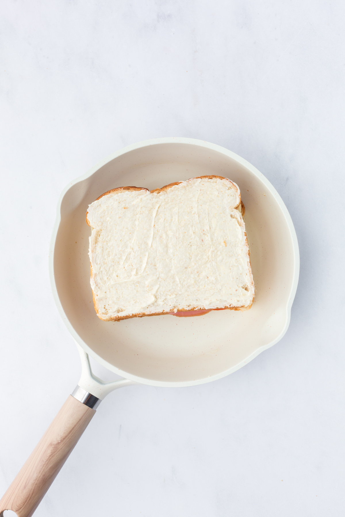 A slice of cheese added and top piece of buttered bread, butter side up.