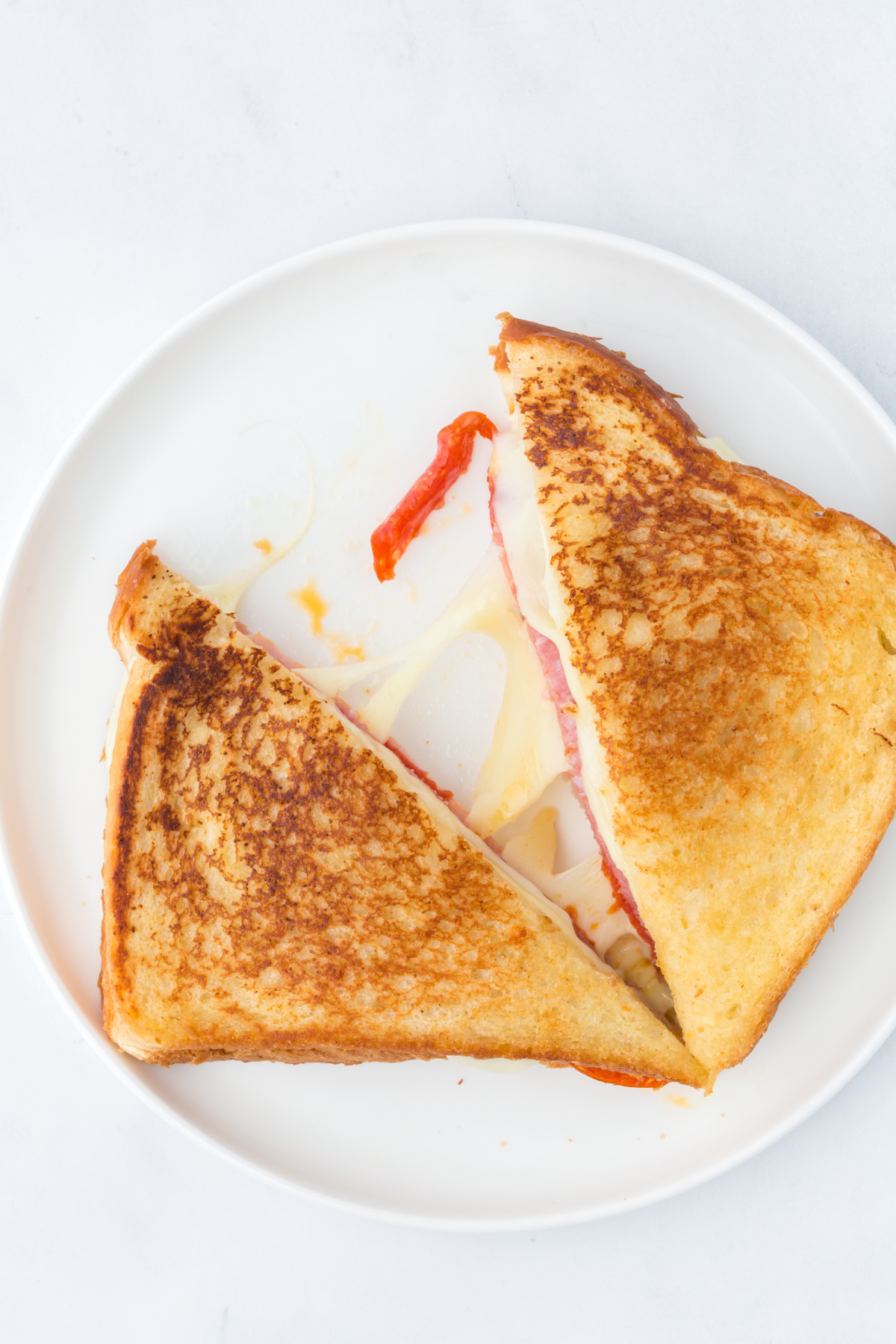 Halved Grilled cheese on a plate with halves separated with melted cheese in between.