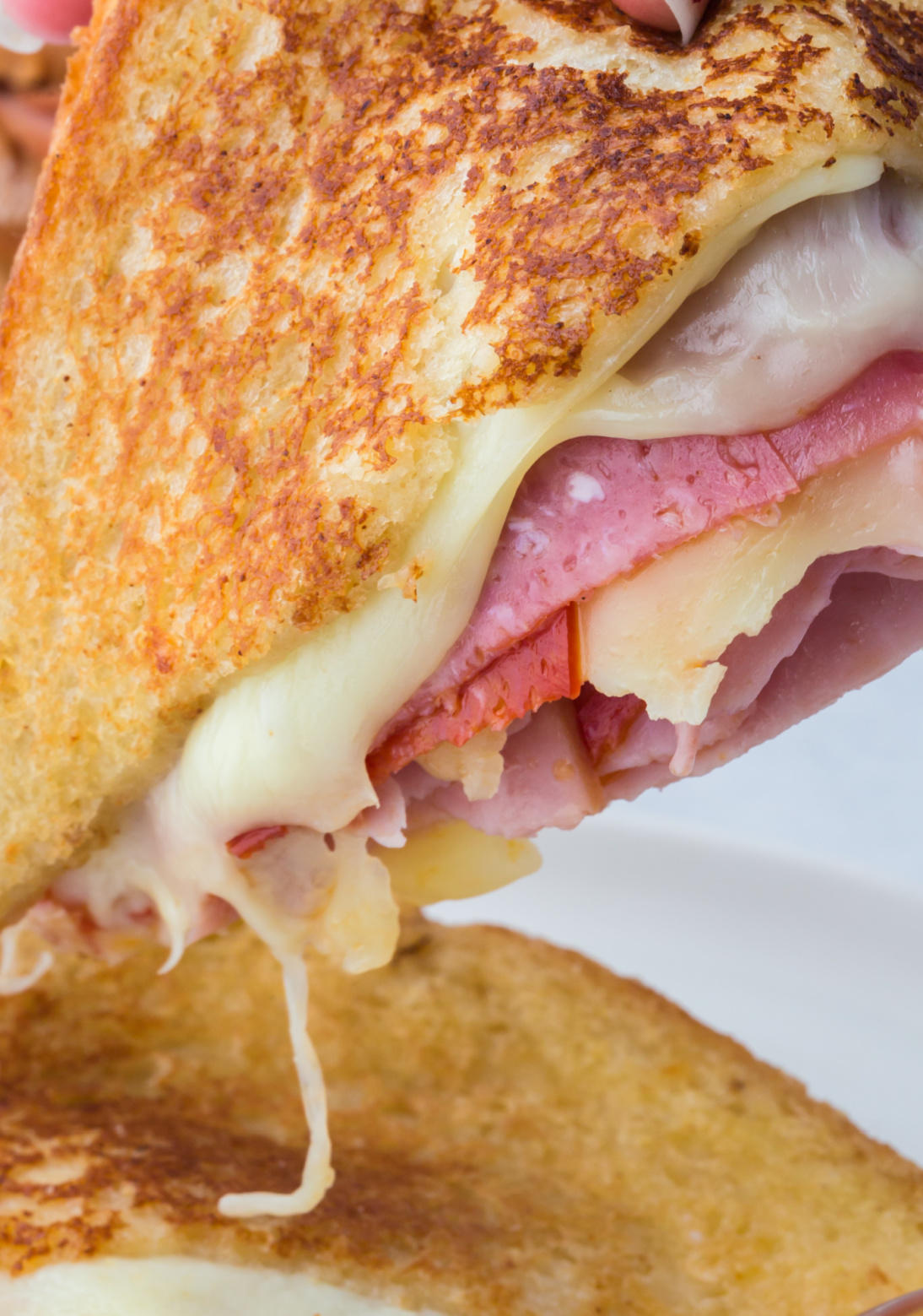 Half of a grilled cheese lifted in the air off the plate ready to take a bite.