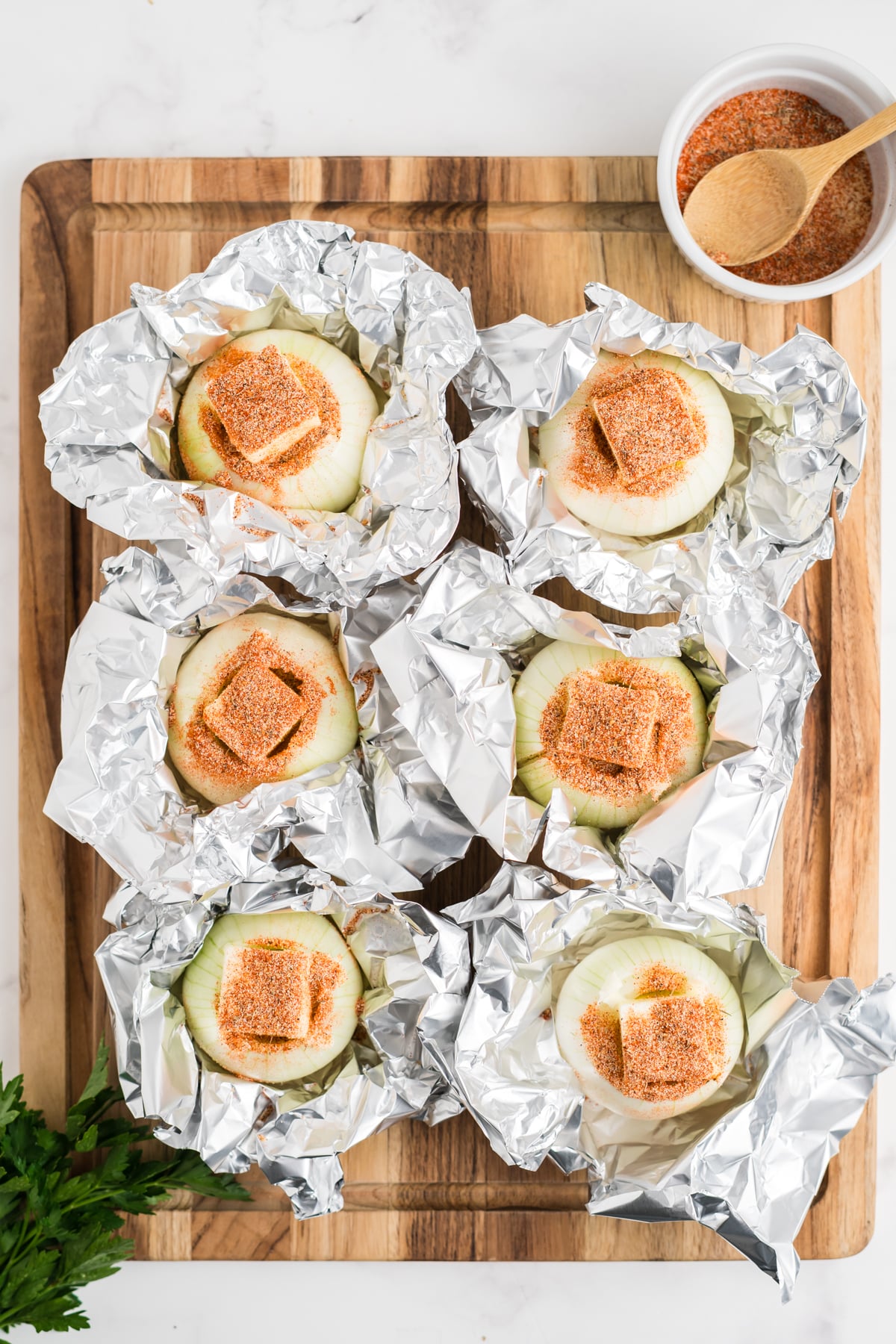 Six onions almost wrapped in foil showing the butter and seasoning mix on top