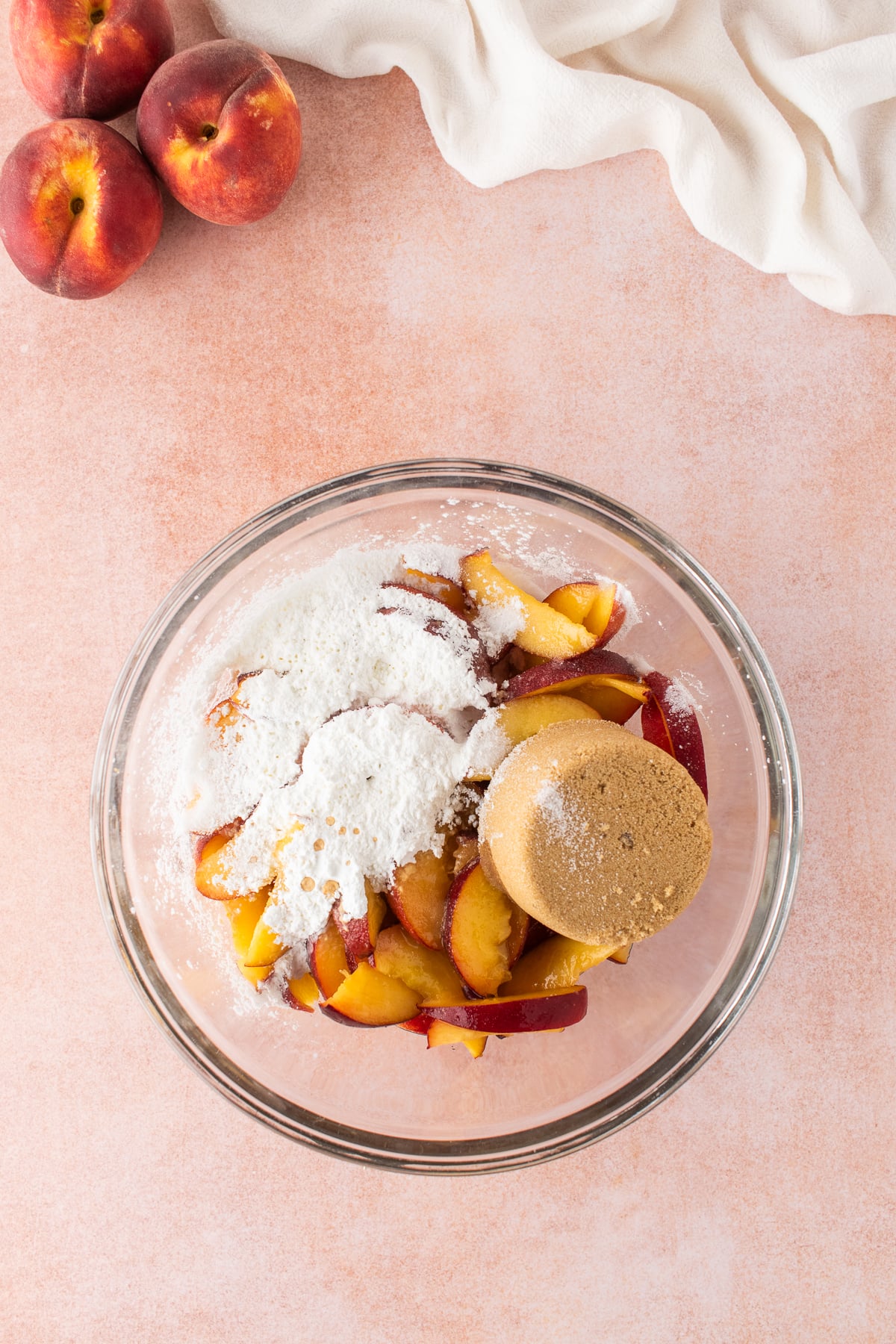 A large bowl of peaches tossed with brown sugar, granulated sugar, cornstarch, lemon juice, vanilla extract, and salt. 