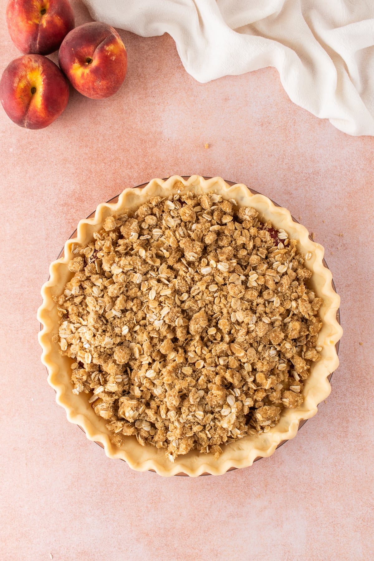 Crumble topping added on top of peaches in pie crust.