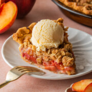 A slice of Peach Crumble Pie on a plate with a scoop of ice cream.