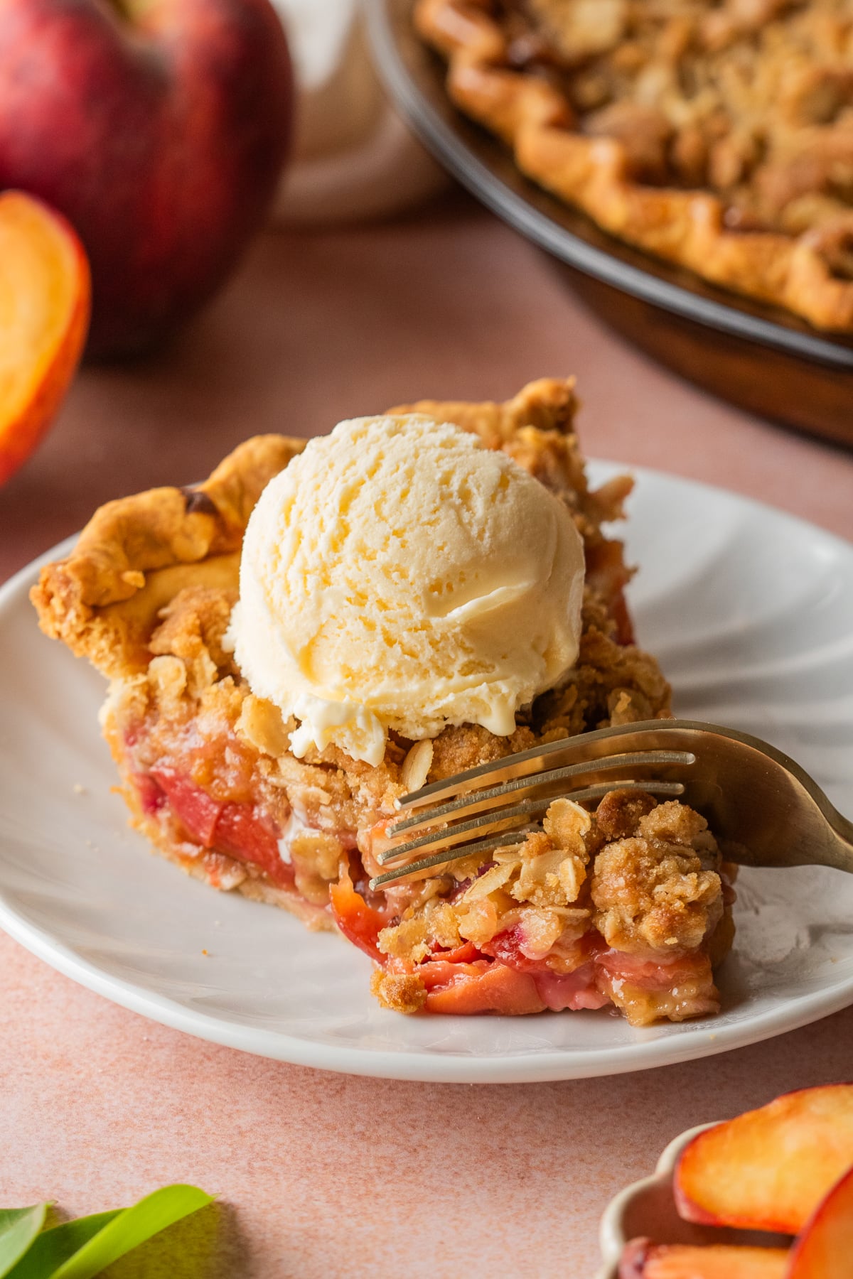 A slice of pie on a plate with a scoop of ice cream and a fork pressing in to remove a bite