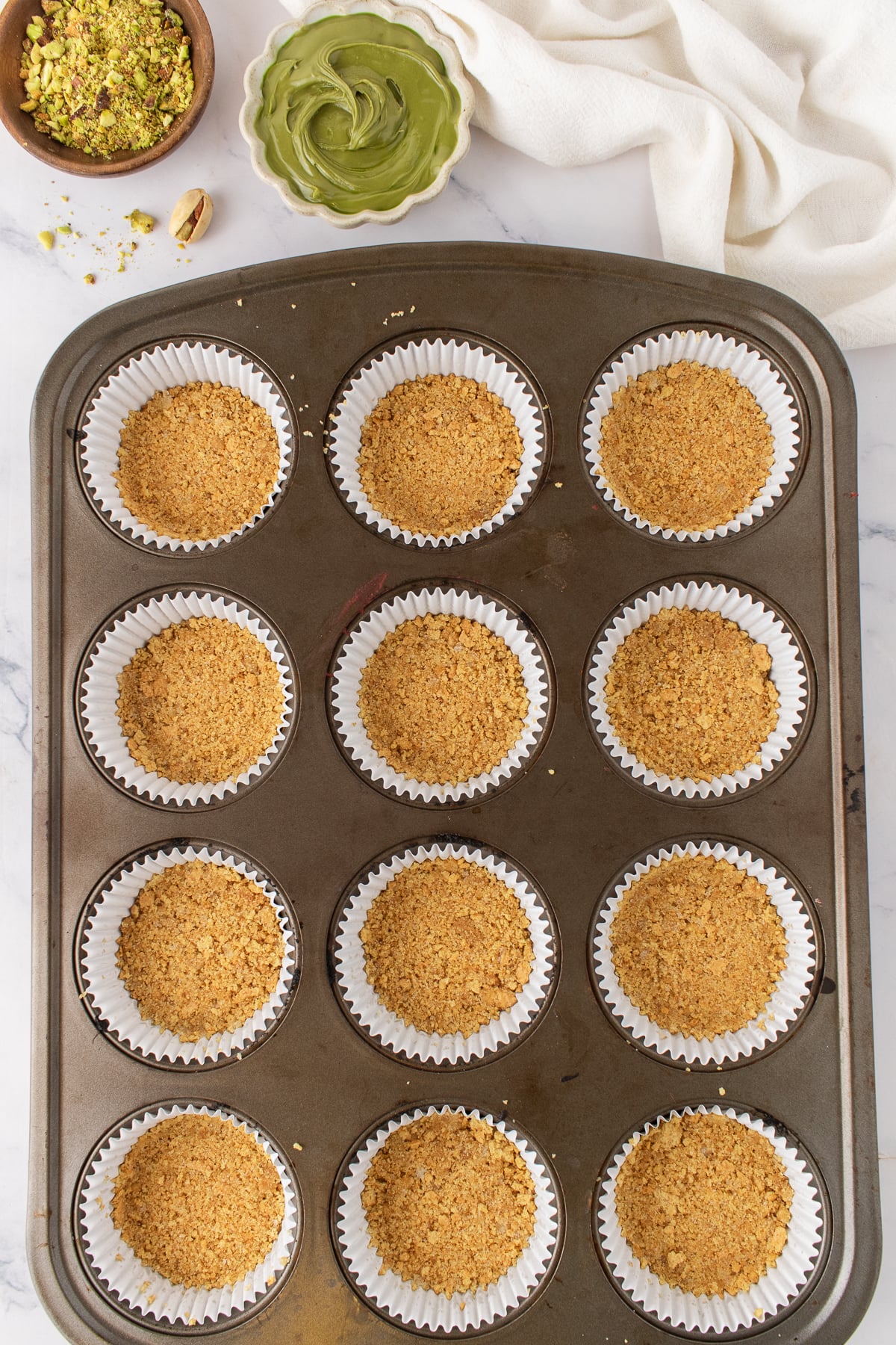 The graham crackers pressed into a muffin tin to form the crust.